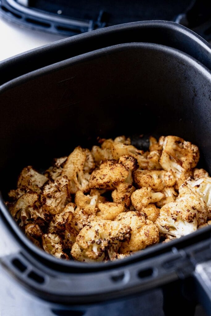 An air fryer basket filled with cooked cauliflower.