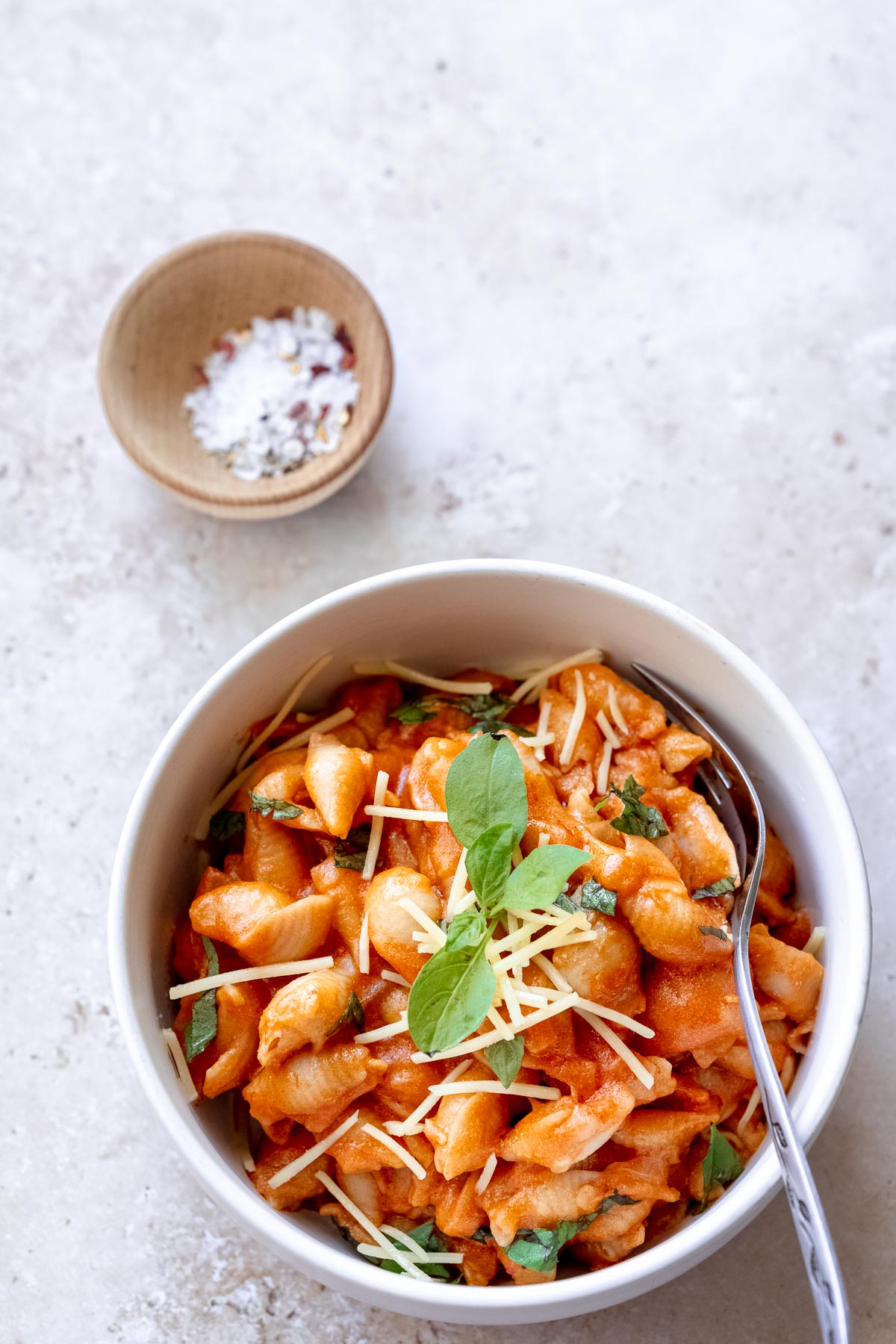 gigi hadid spicy vodka pasta sauce recipe in a white bowl filled with shell noodles, cheese and basil.