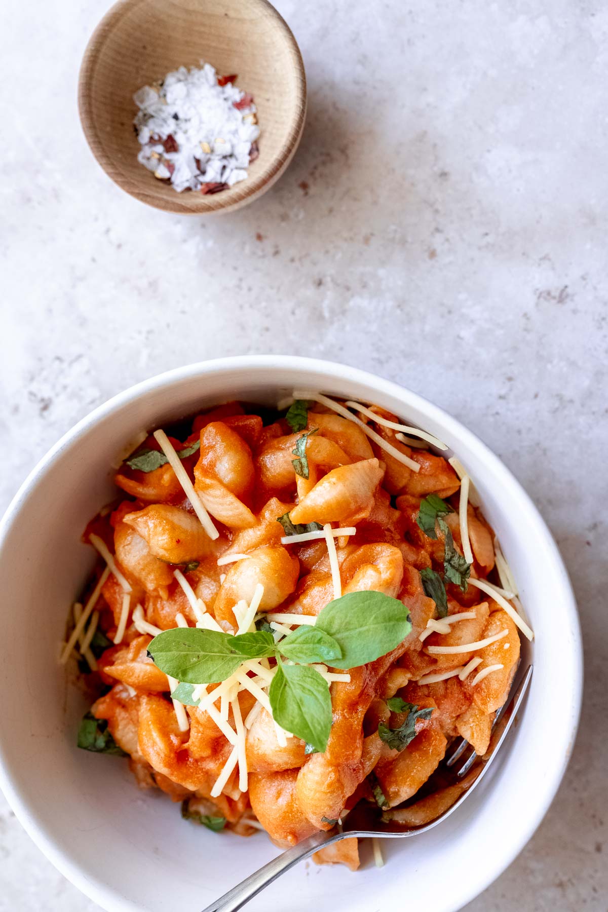 a close shot of gigi hadid pasta recipe in a white ceramic bowl garnished with parmesan cheese and fresh basil leaves.