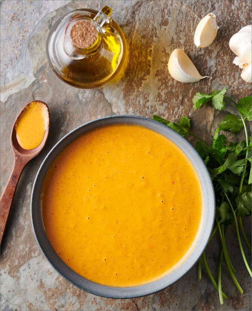 vibrant orange peri peri sauce recipe in a dark bowl from hot sauce cookbook for beginners from kristen wood.