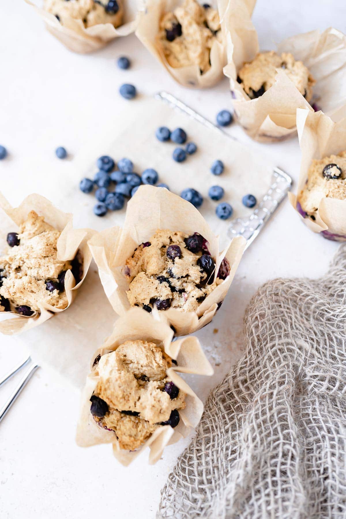 gluten free vegan blueberry muffins wrapped in bakery paper scattered with fresh plump blueberries.