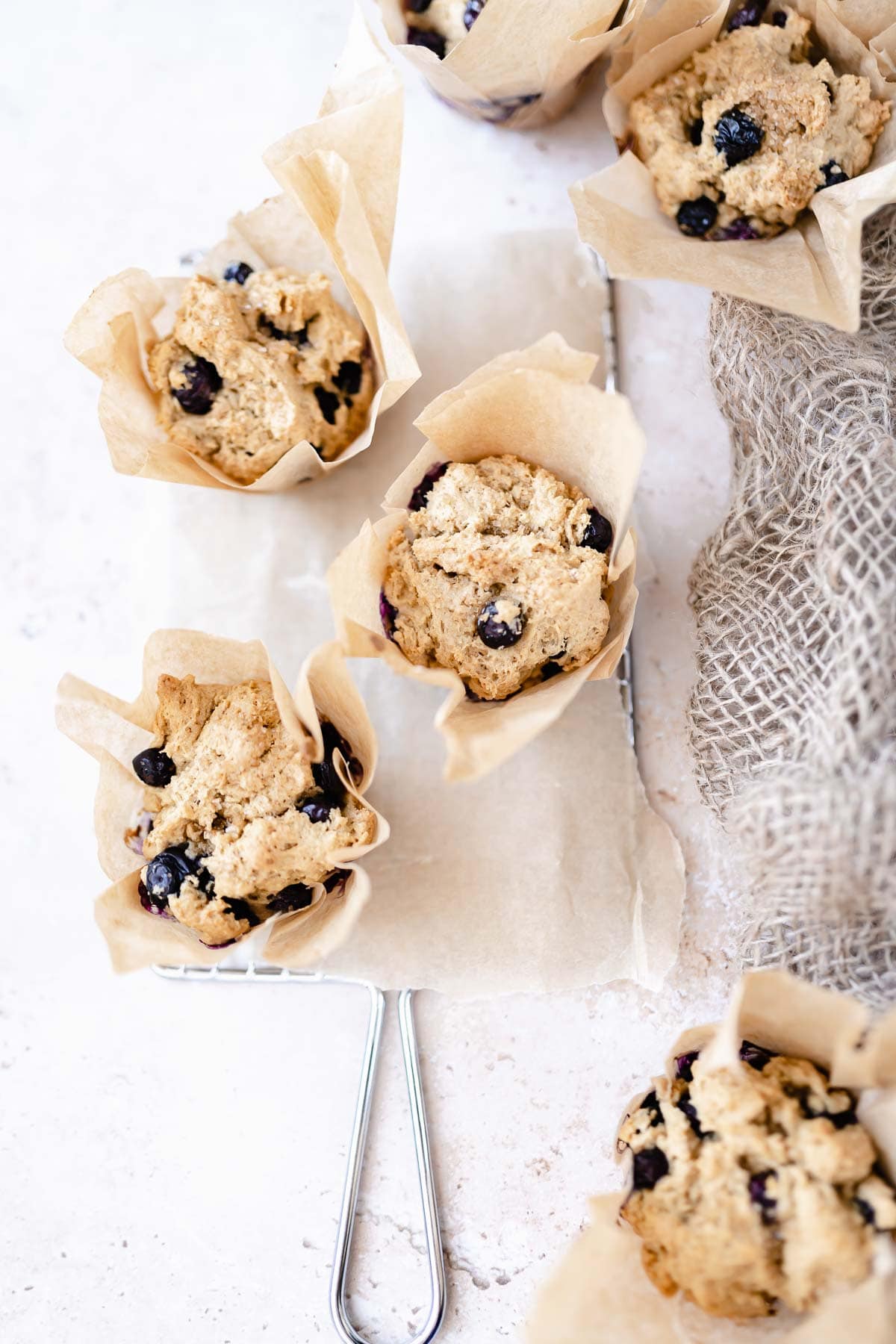 a wire rack with gluten free blueberry muffins stacked about wrapped in brown parchment paper.