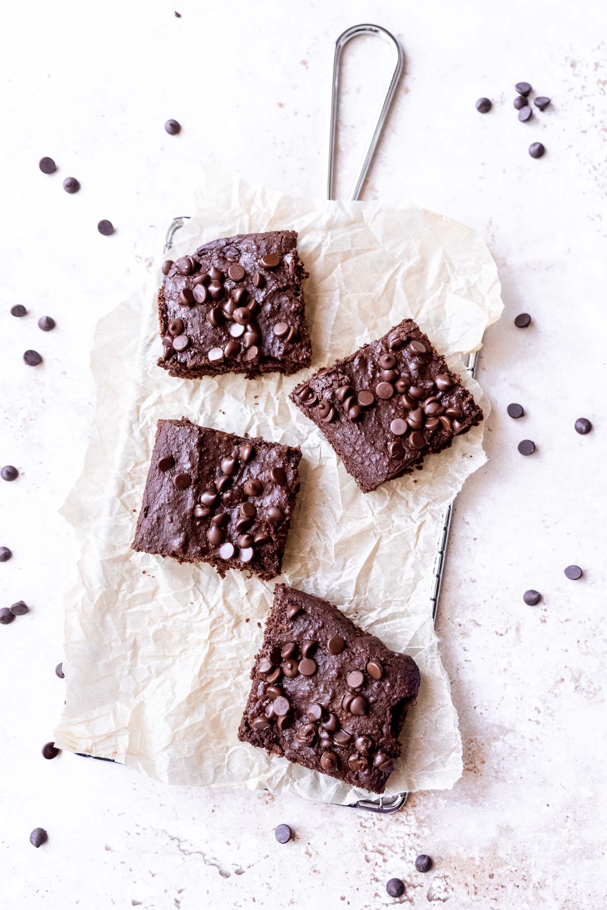 fudgy black bean brownies resting on crumpled parchment paper sprinkled with chocolate chips.
