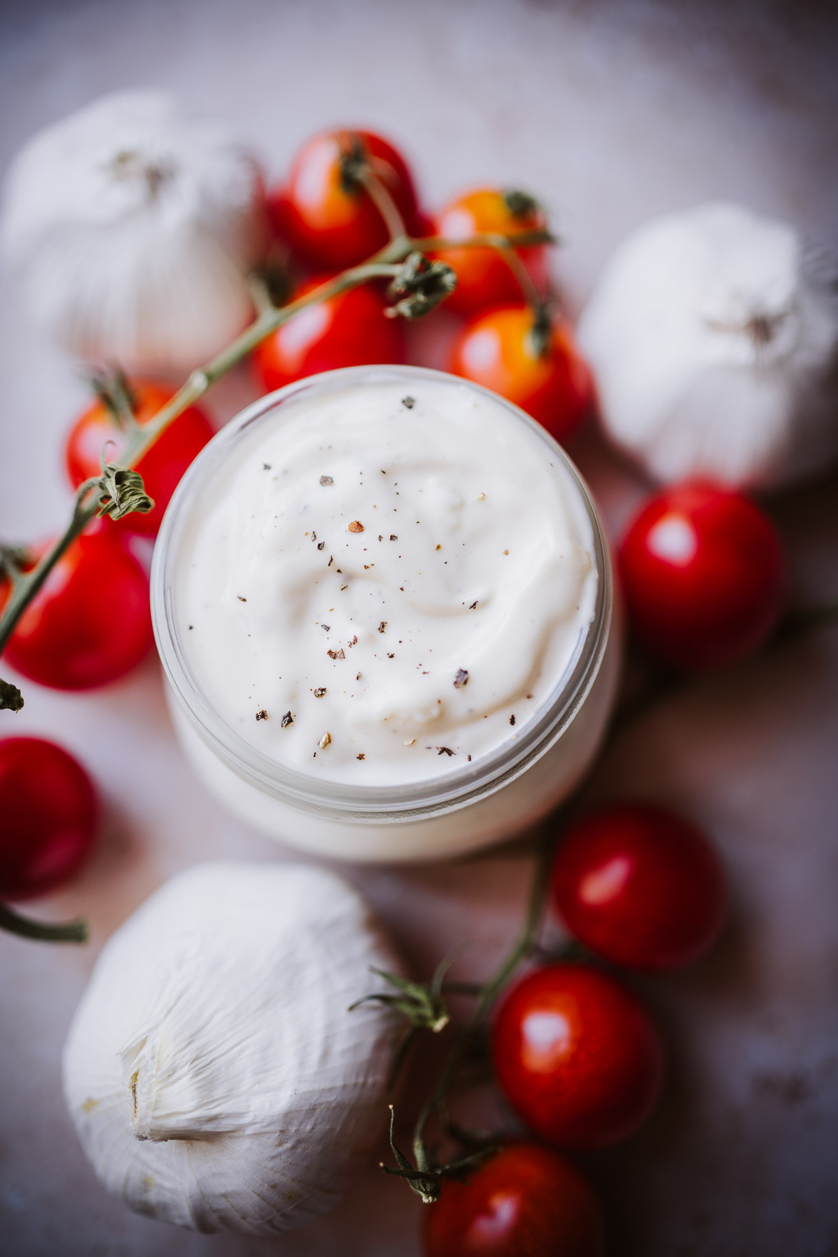 creamy white pizza aioli sauce in a clear jar dusted with freshly ground black pepper.