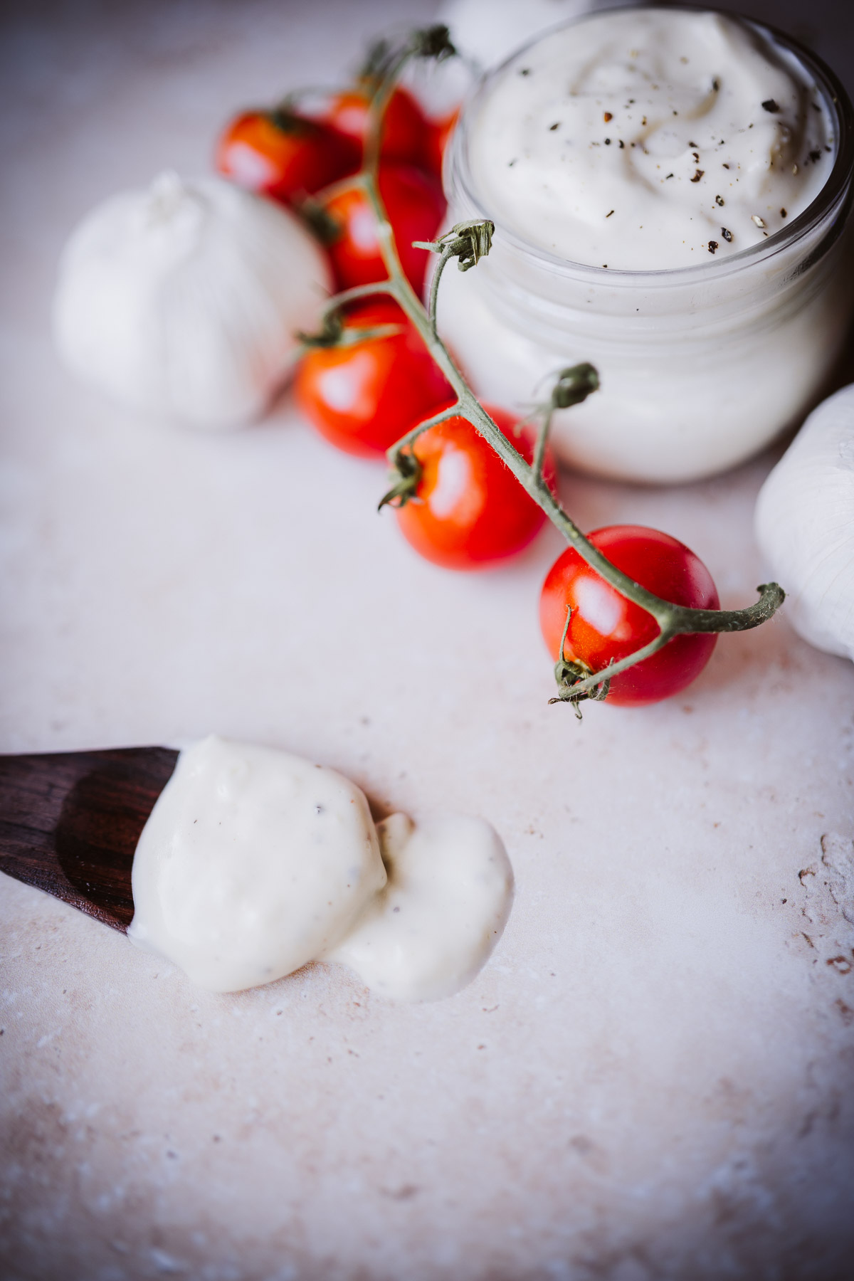 white creamy pizza aioli sauce in a small glass jar resting next to tomatoes on the vine.