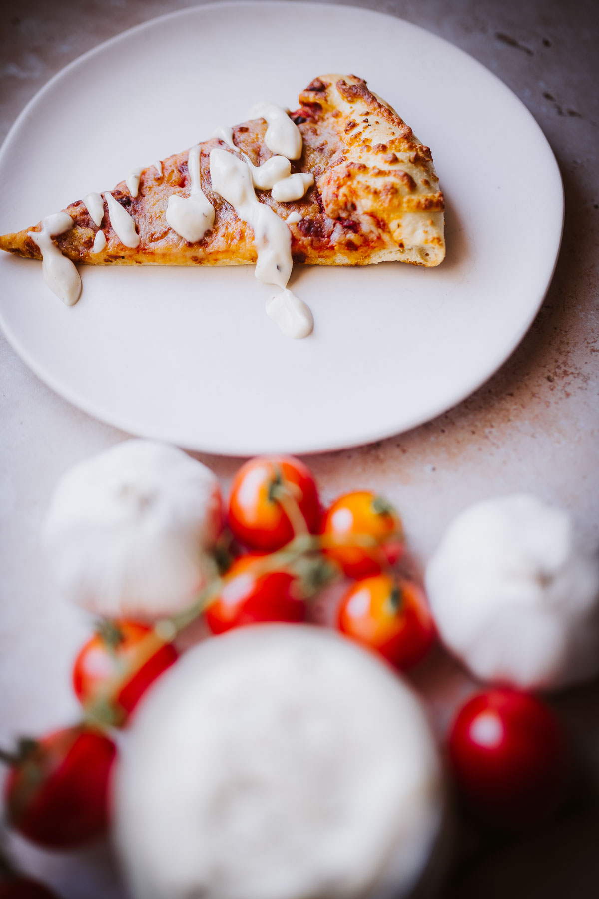 a garlic aioli sauce drizzled over a slice of cheese pizza on a white plate.