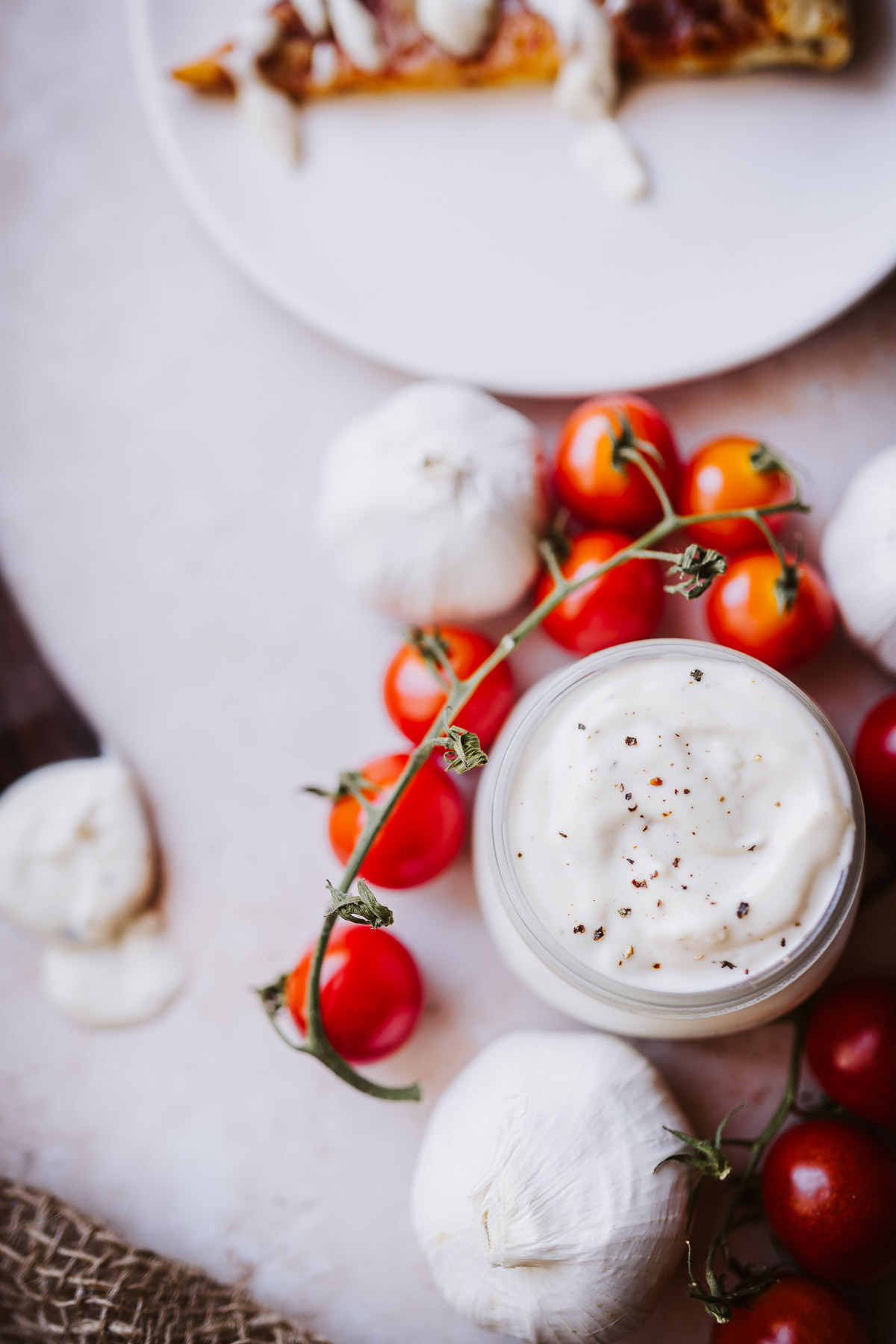 fresh pizza aioli sauce surrounded by tomatoes and heads of garlic.