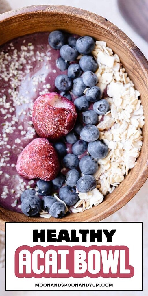 A wooden bowl filled with a vibrant acai bowl smoothie, blueberries, frozen strawberries, oats, and hemp seeds sits on a light surface. Text reads "Healthy Acai Bowl.