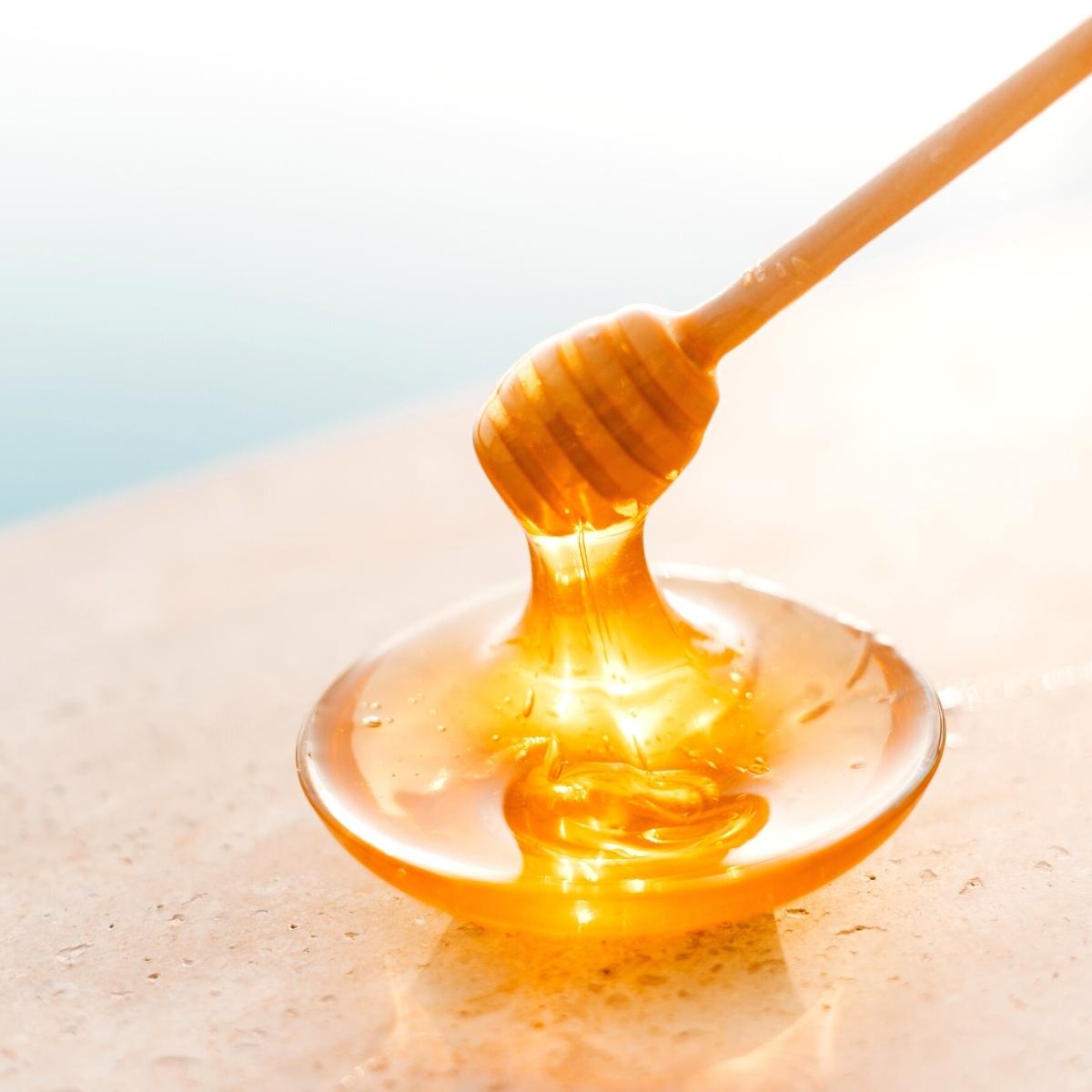 fresh raw honey dripping from a wooden honey spoon glistening in the sunlight.
