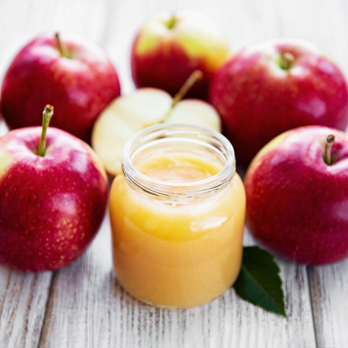 a jar of applesauce surrounded by redapples.