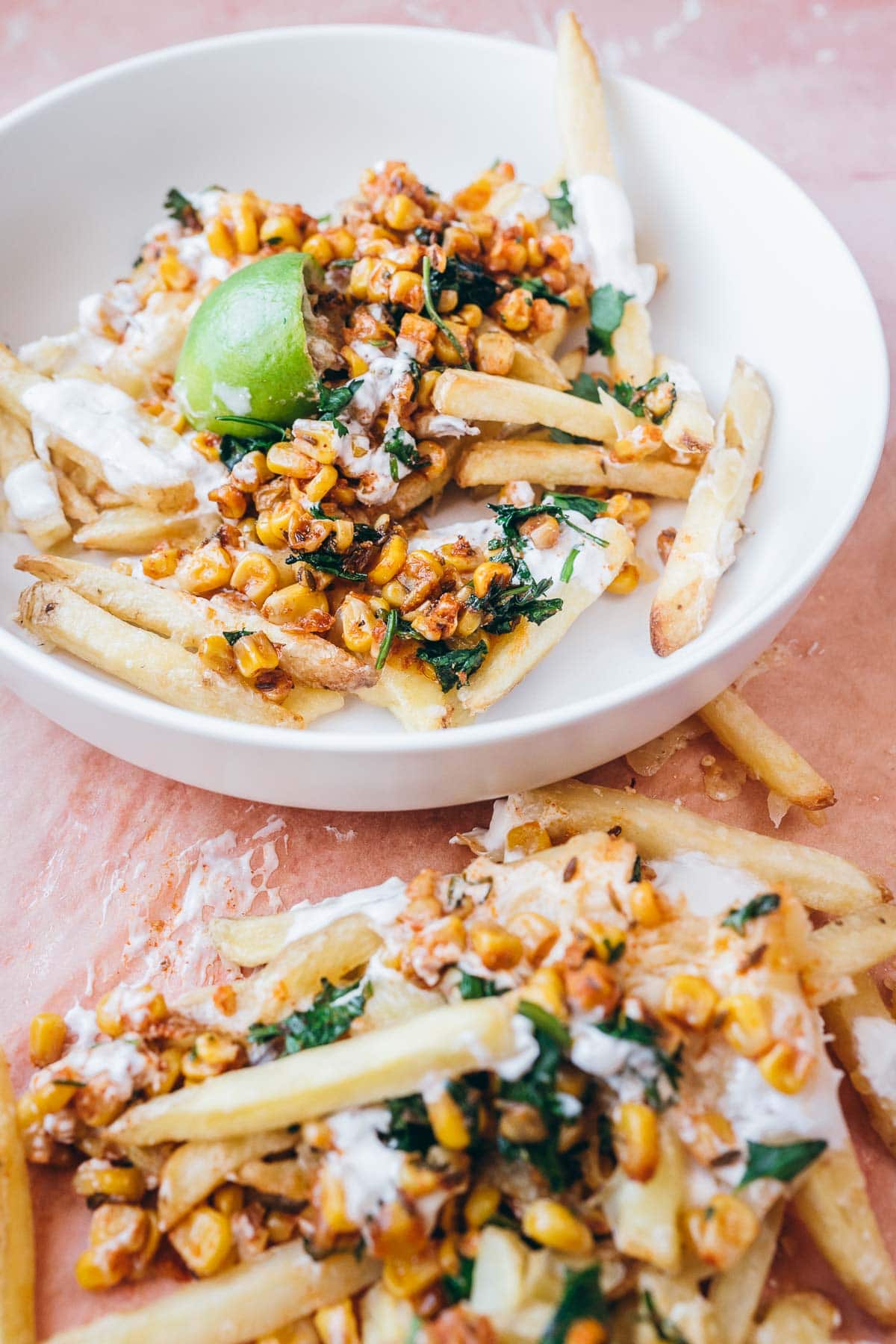 a white bowl filled with french fries topped with cheese, corn, cilantro, fresh lime and sour cream.