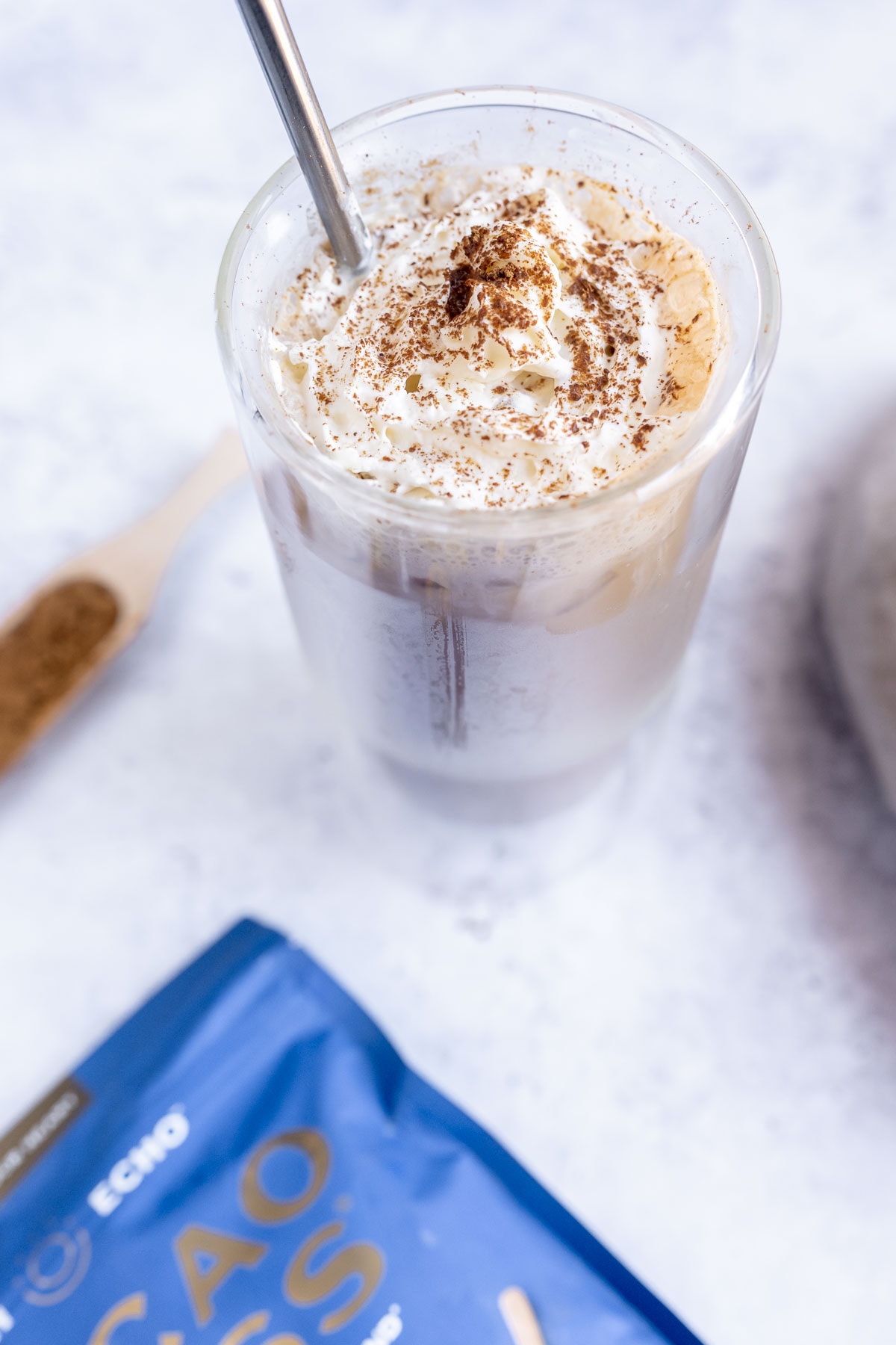 tall clear glass of peanut butter latte topped with whipped cream and cacao powder.