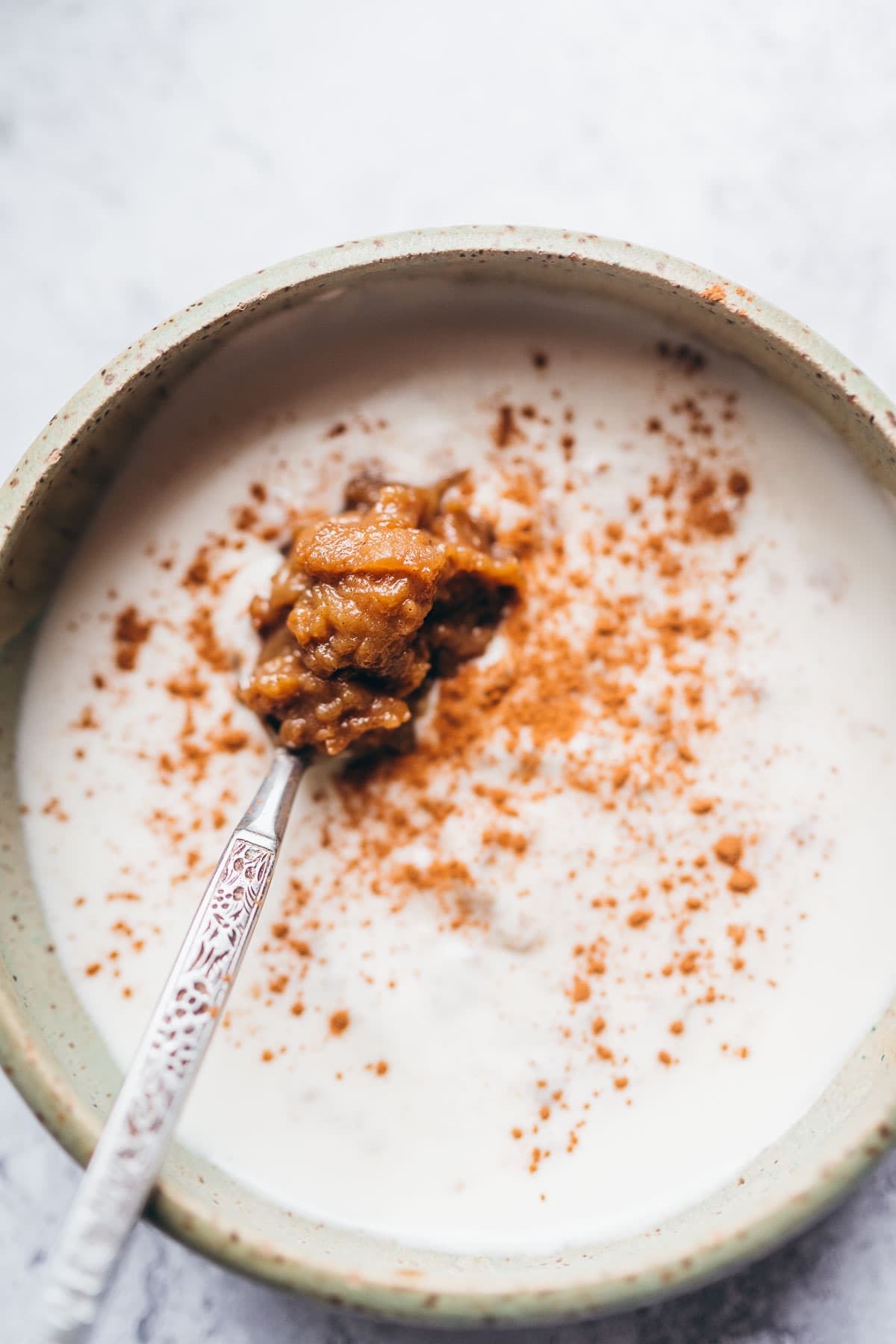 top view of green ceramic bowl filled with white yogurt, a dollop of apple curd and sprinkle of ground cinnamon.