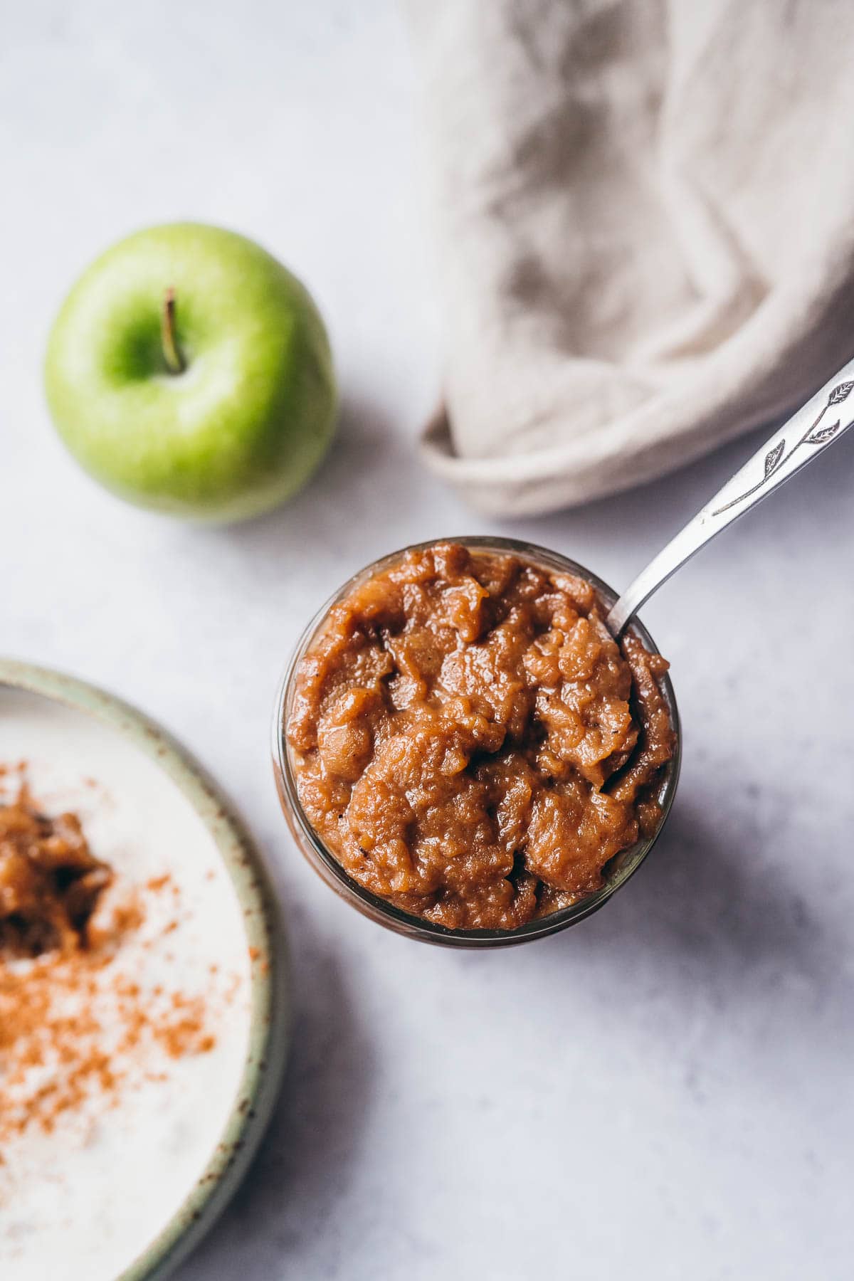 a jar of apple curd next to a bowl of yogurt and a green apple.