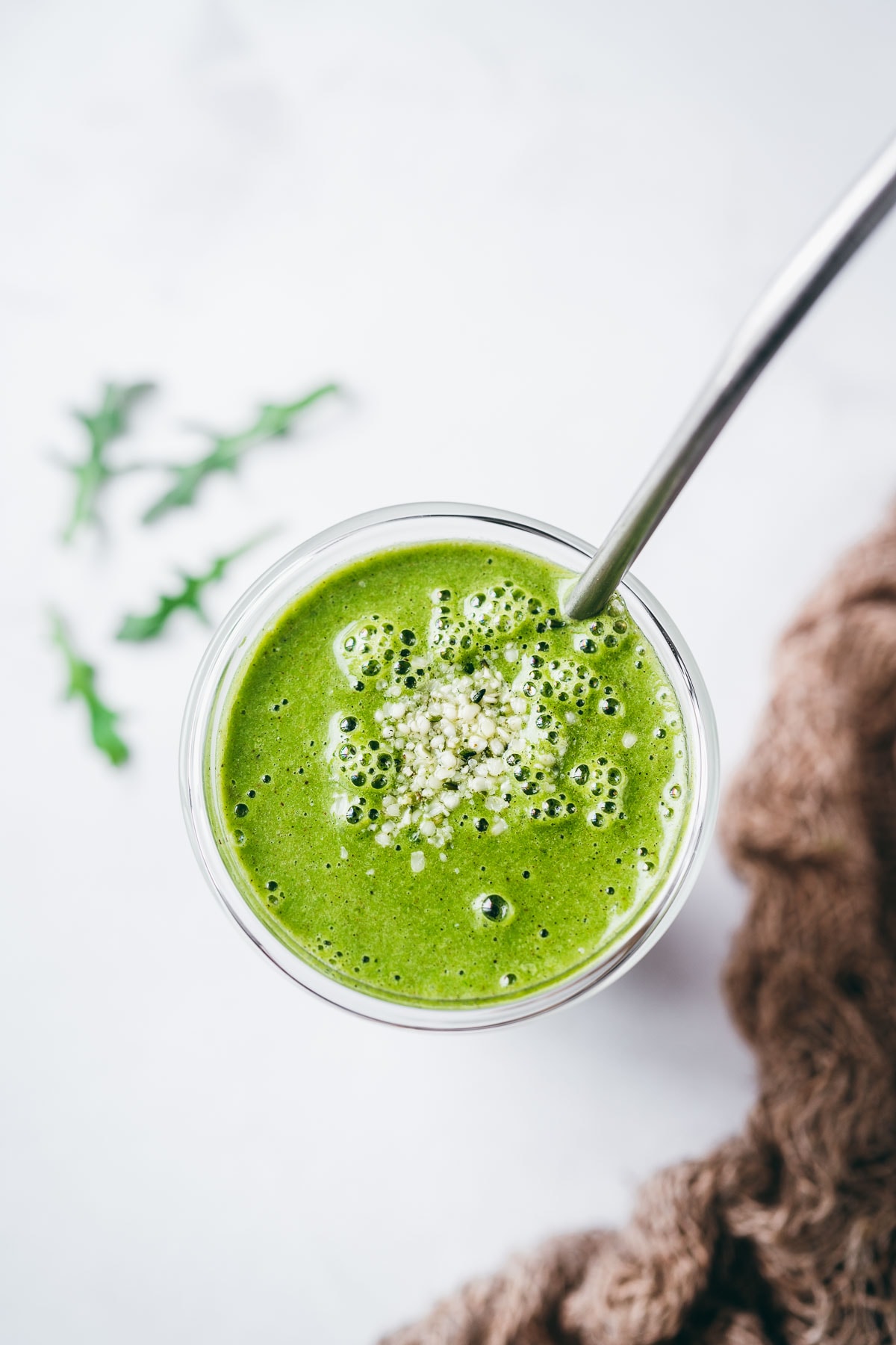 top view of a bright green drink in a clear glass garnished with small white seeds.