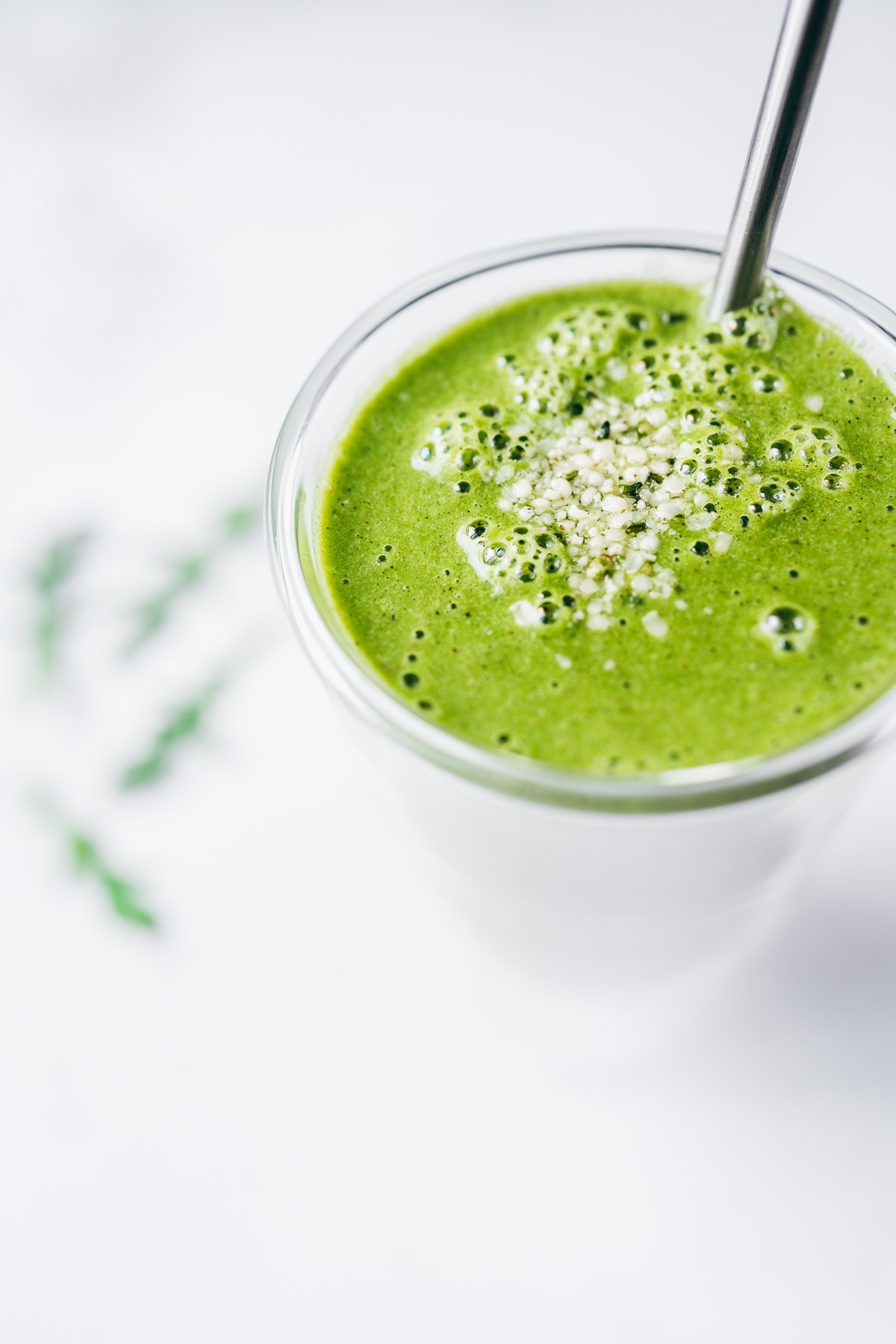 a close side view of a vibrant green arugula smoothie topped with white hemp seeds.