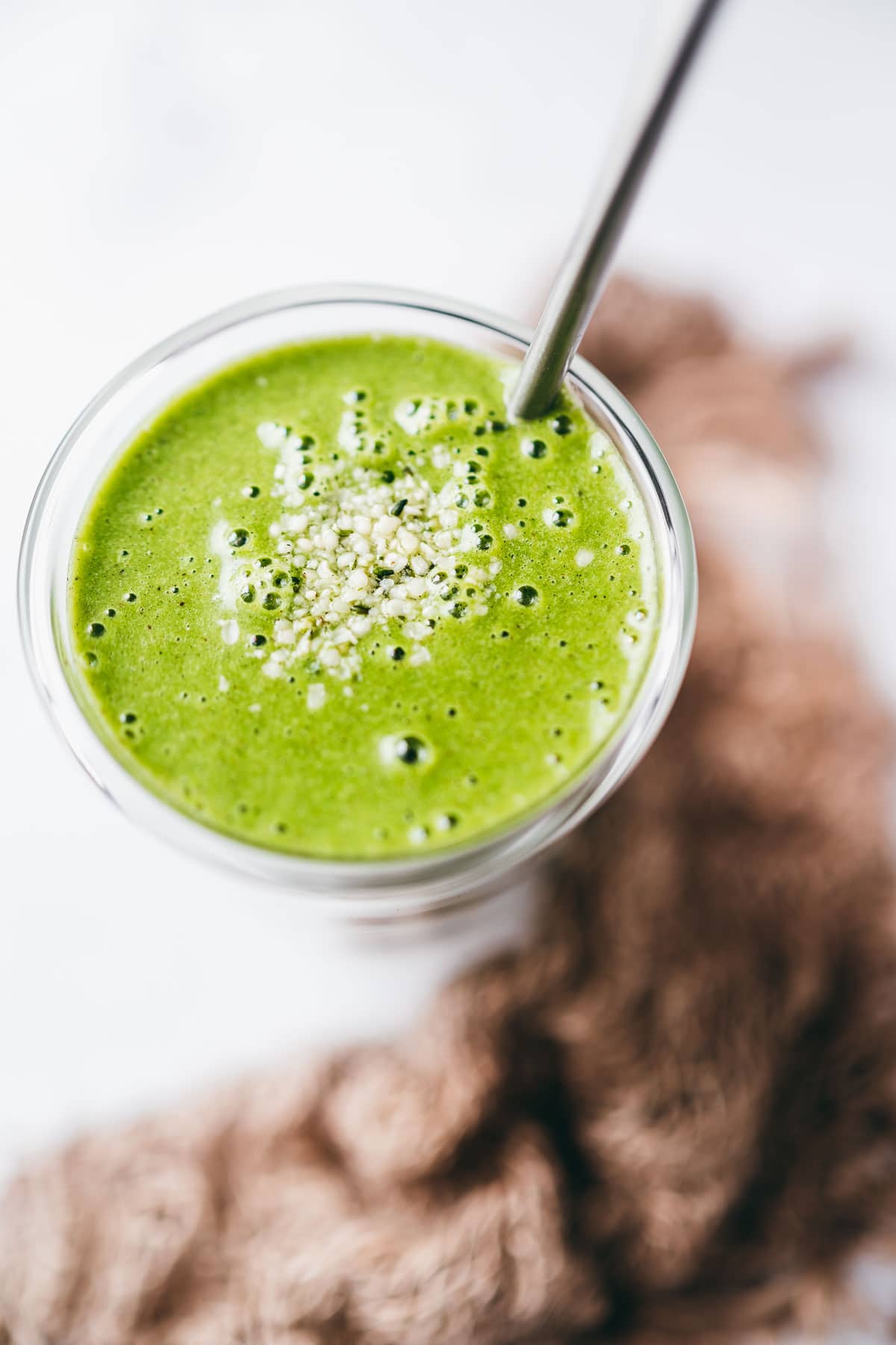 close view of bubbly green smoothie recipe topped with small white hemp seeds.