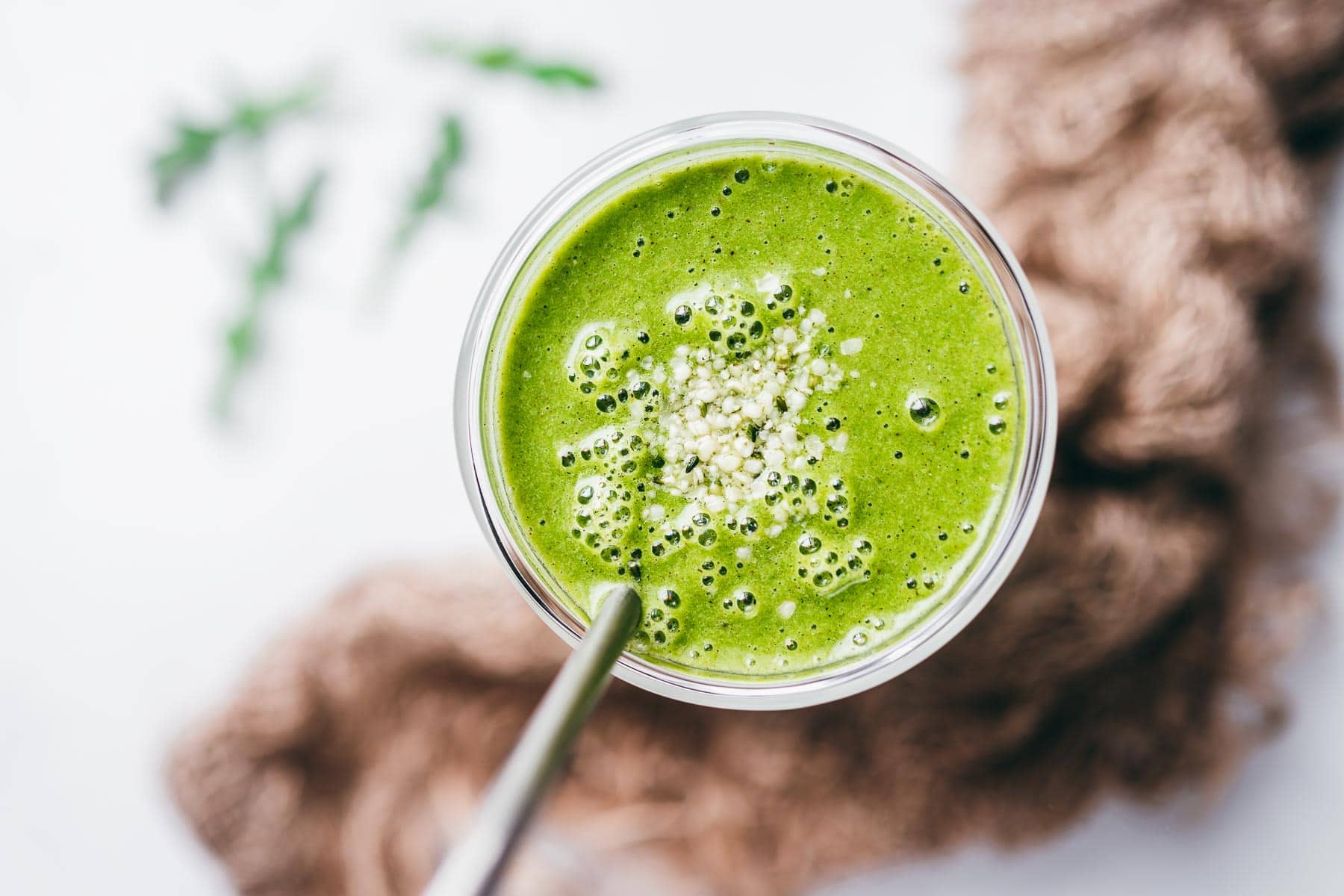 bubbly vibrant green arugula smoothie in a tall clear glass garnished with seeds and a tall stainless steel straw.