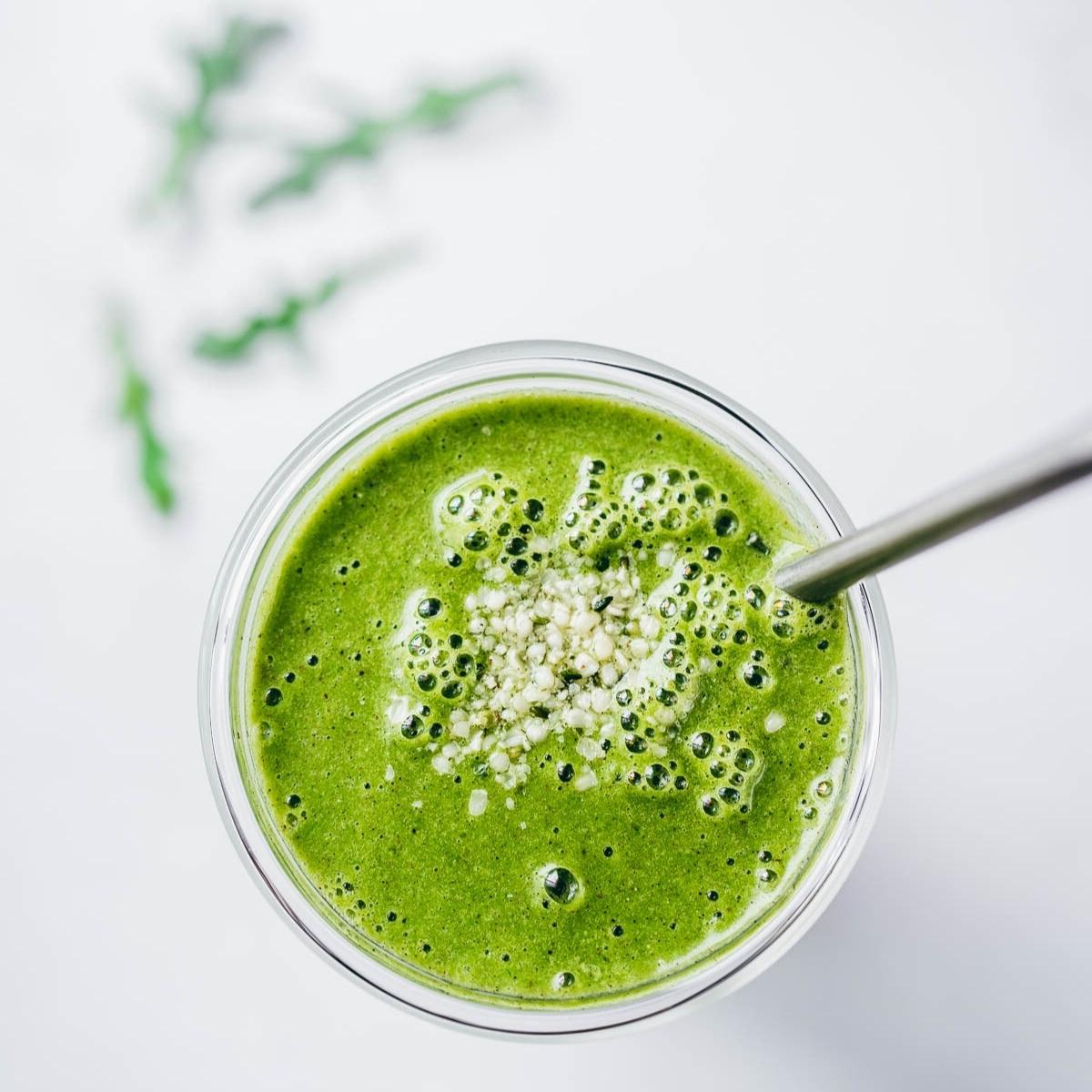 top view of a bright green smoothie in a clear glass topped with a sprinkle of hemp seeds.