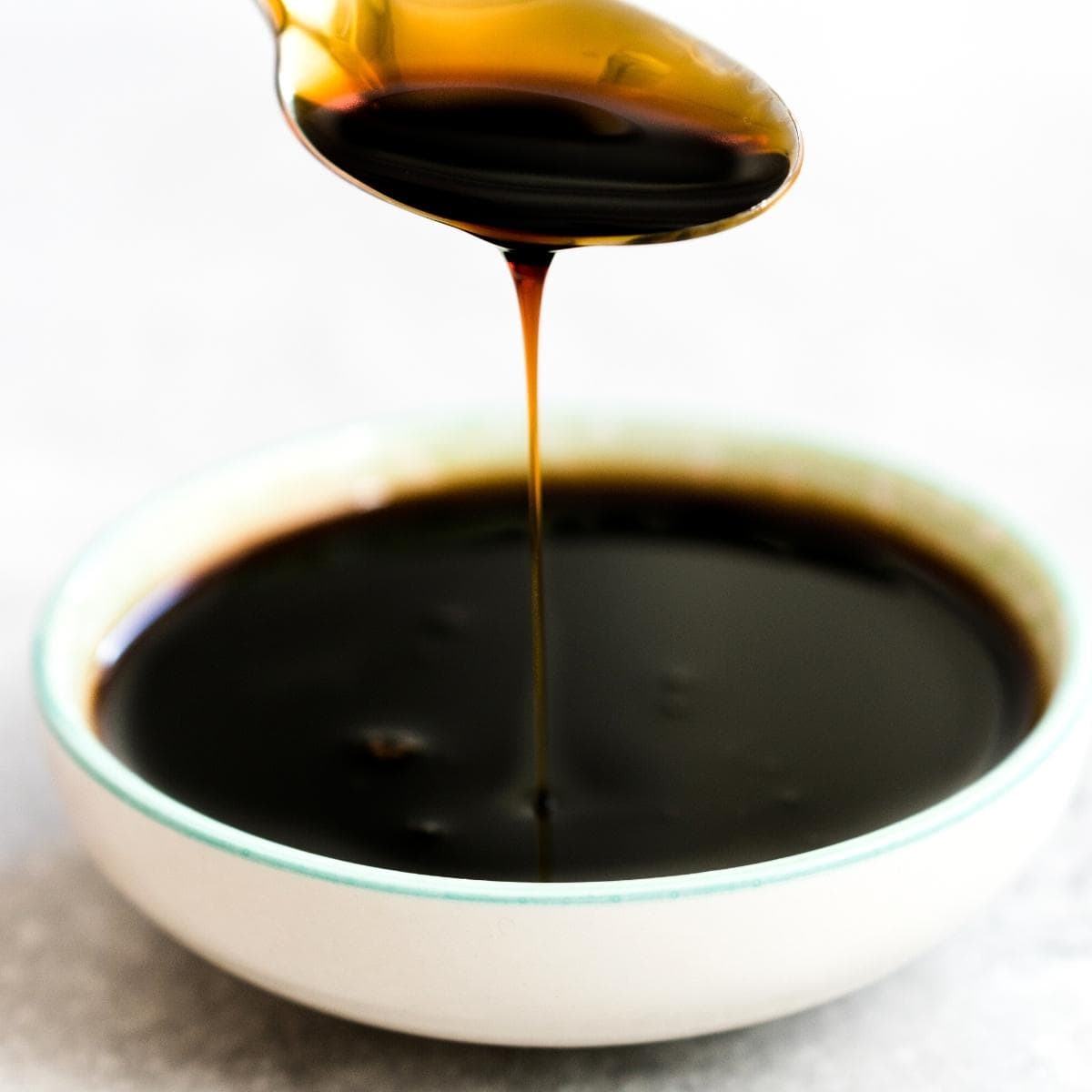 a spoon drizzling molasses into a white bowl.