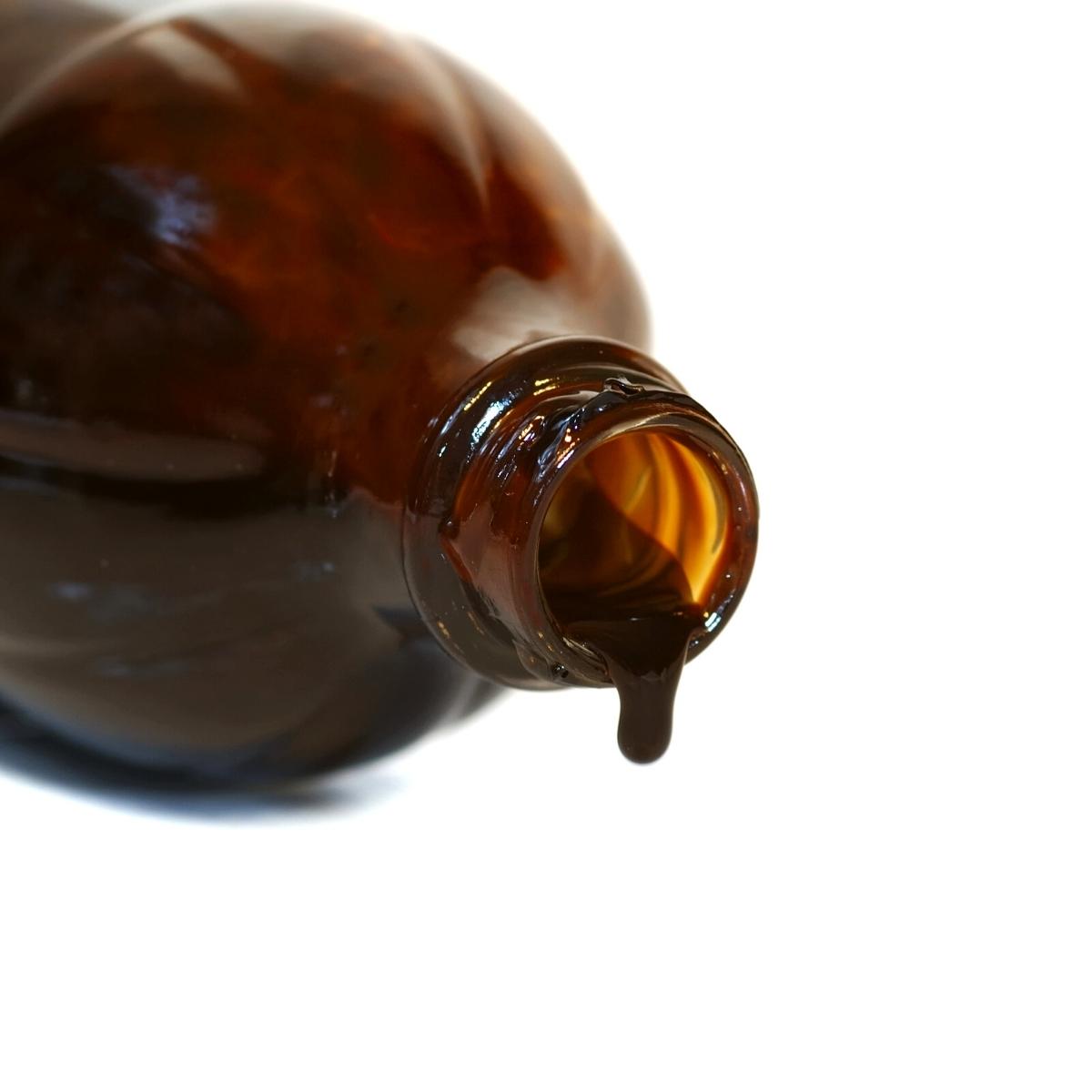 a close up shot of a dark bottle with molasses dripping from the opening.