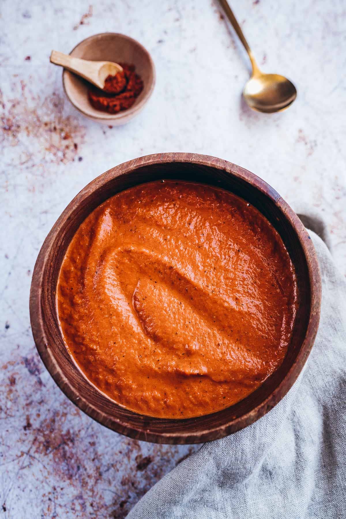 swirls of orange red bravas sauce fill a dark wooden bowl.
