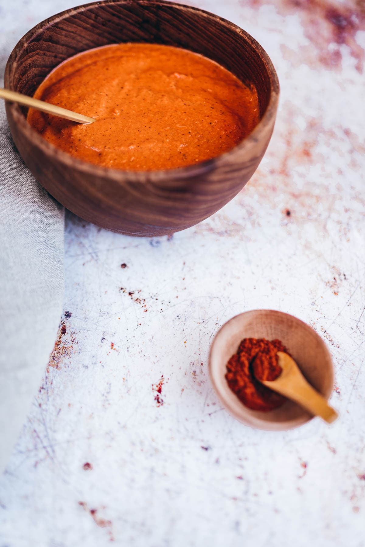 a gold spoon juts out of dark wooden bowl filled with a rich red spanish bravas sauce.