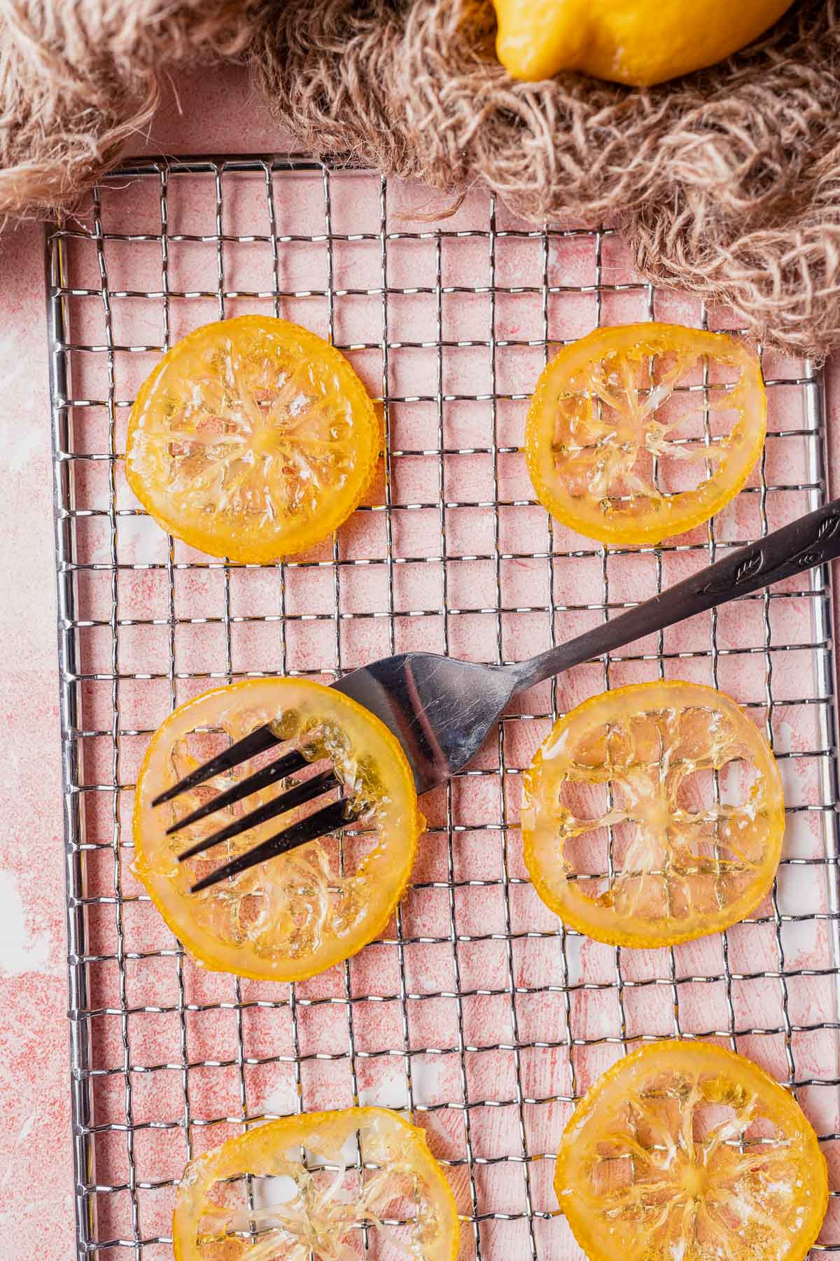 A silver fork pokes through a candied lemon on a wire rack.