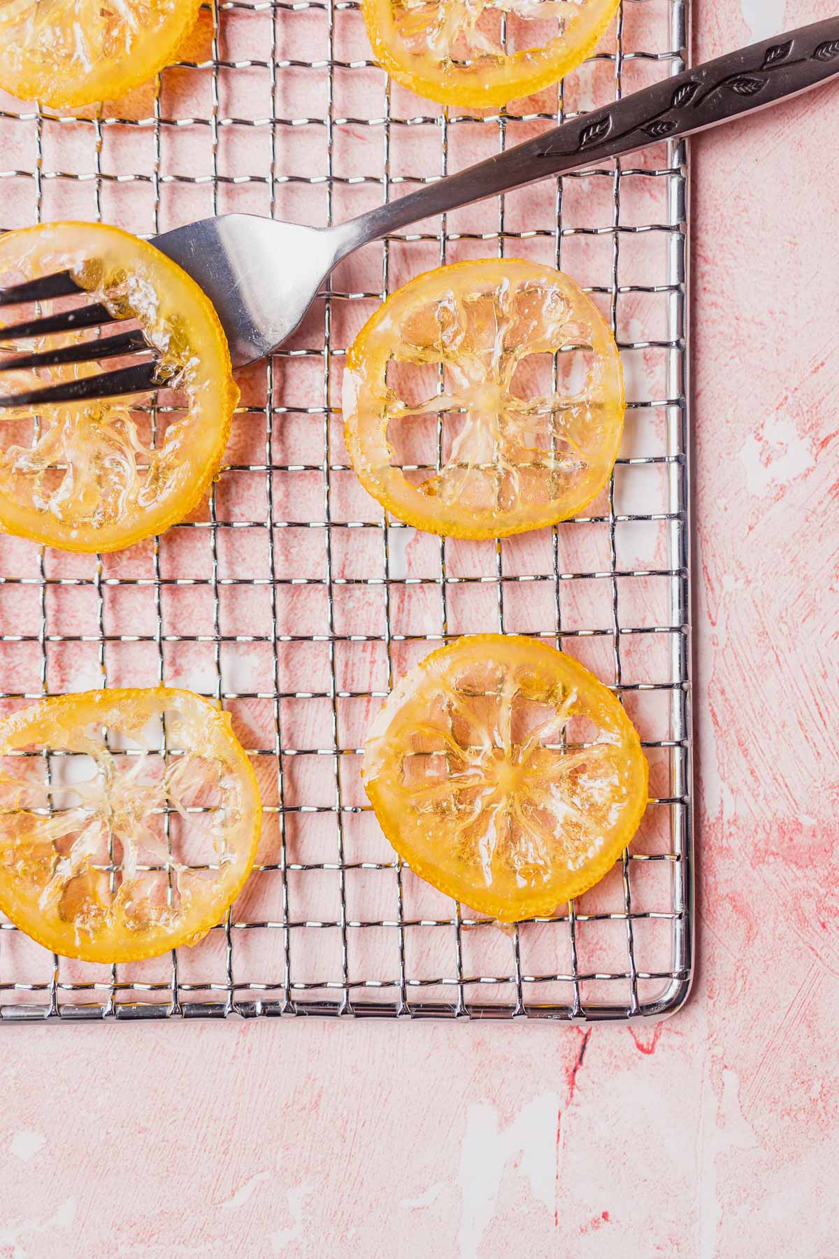 A silver rack topped with slices of candied lemons and silver fork resting through one.