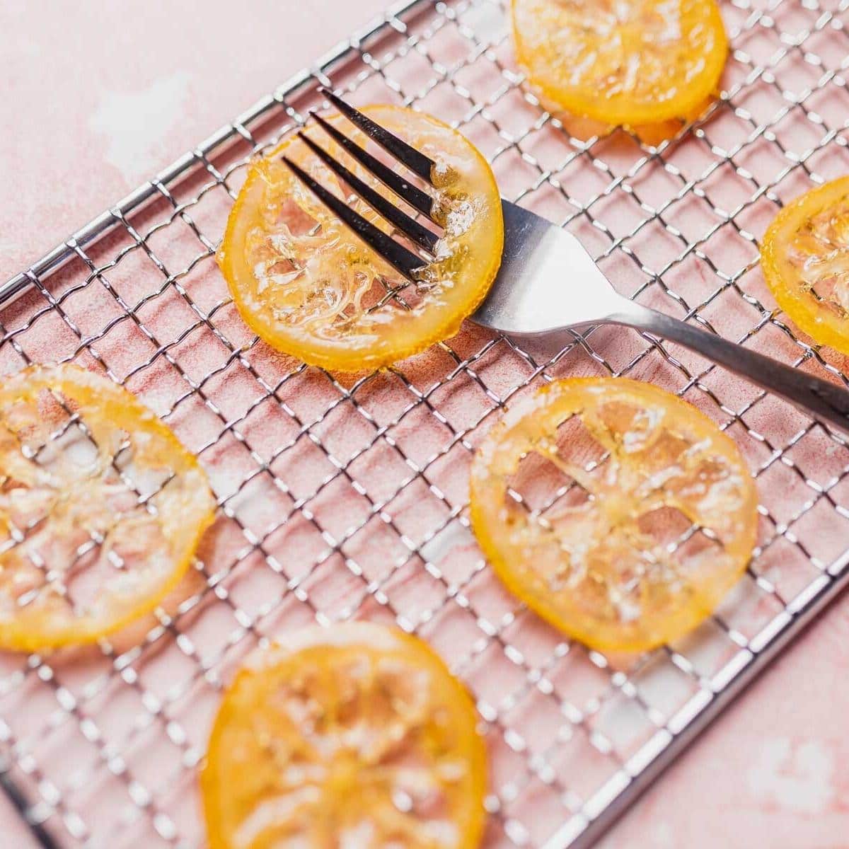 Candied lemon slices resting on a silver metal rack with a silver spoon poking through one of them.