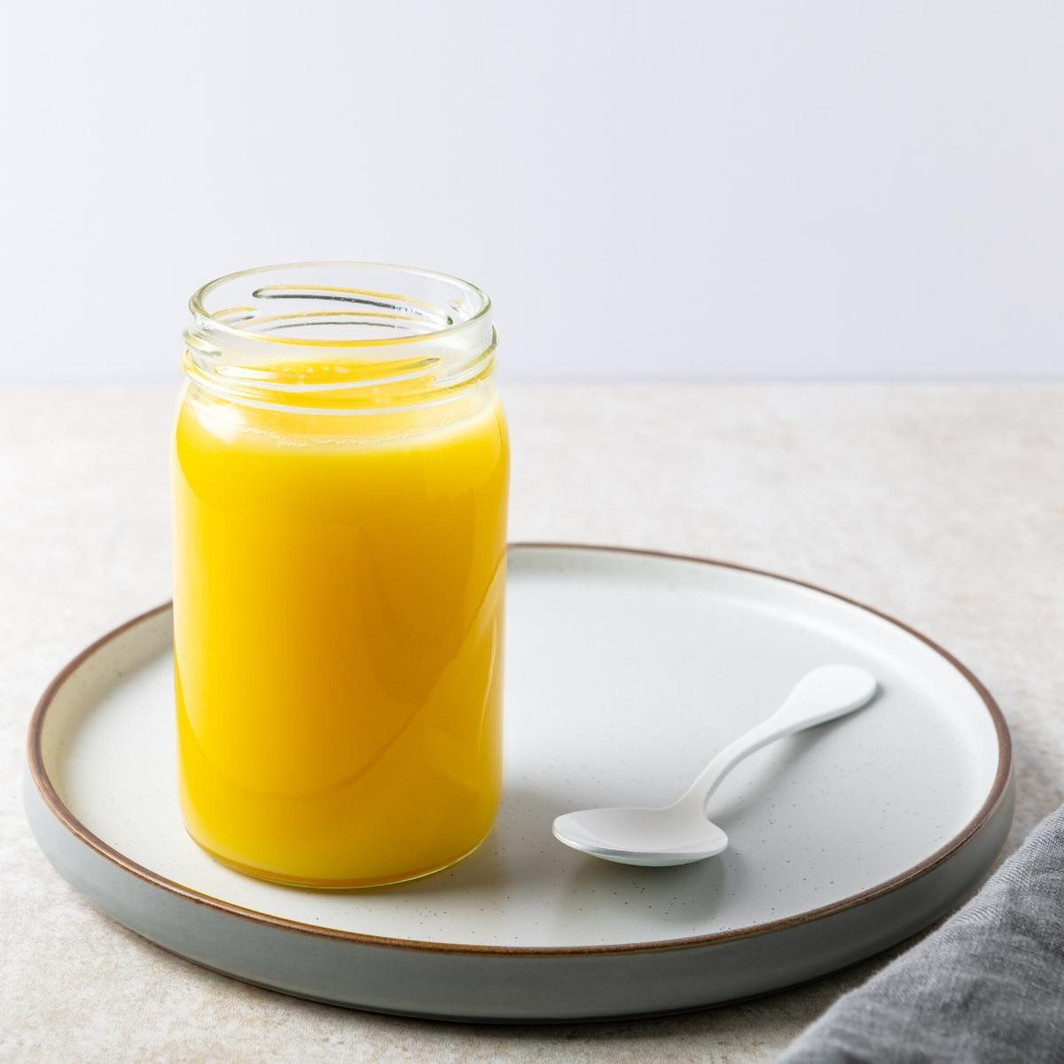 a jar of ghee aka clarified butter resting on a ceramic plate next to a silver spoon.