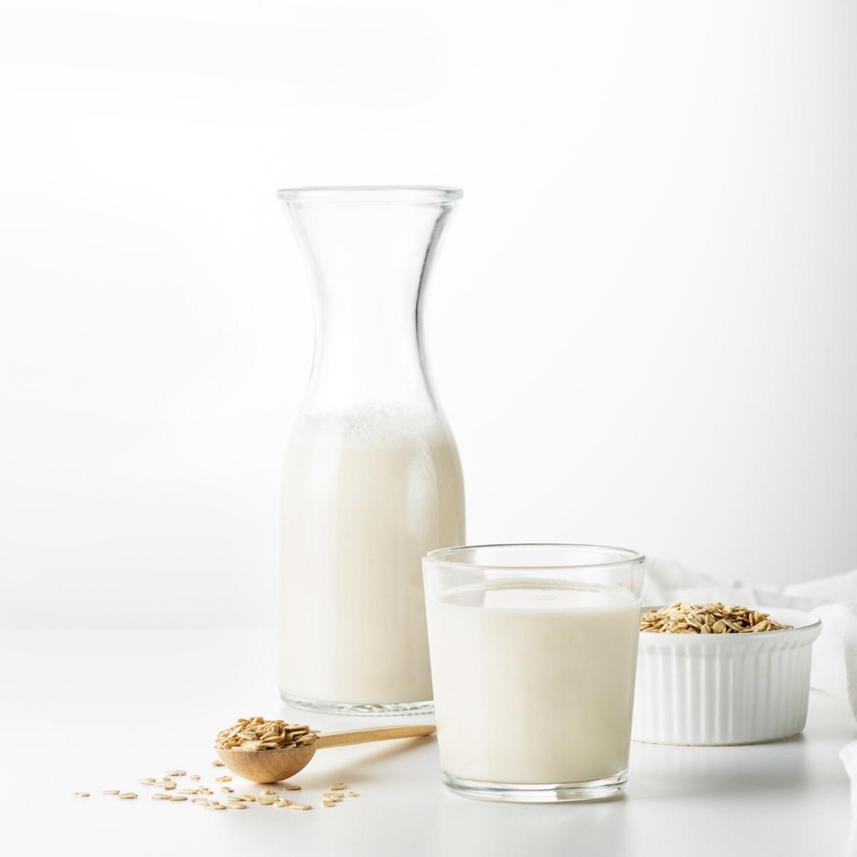 Two clear glasses filled with white oat milk on a white table.