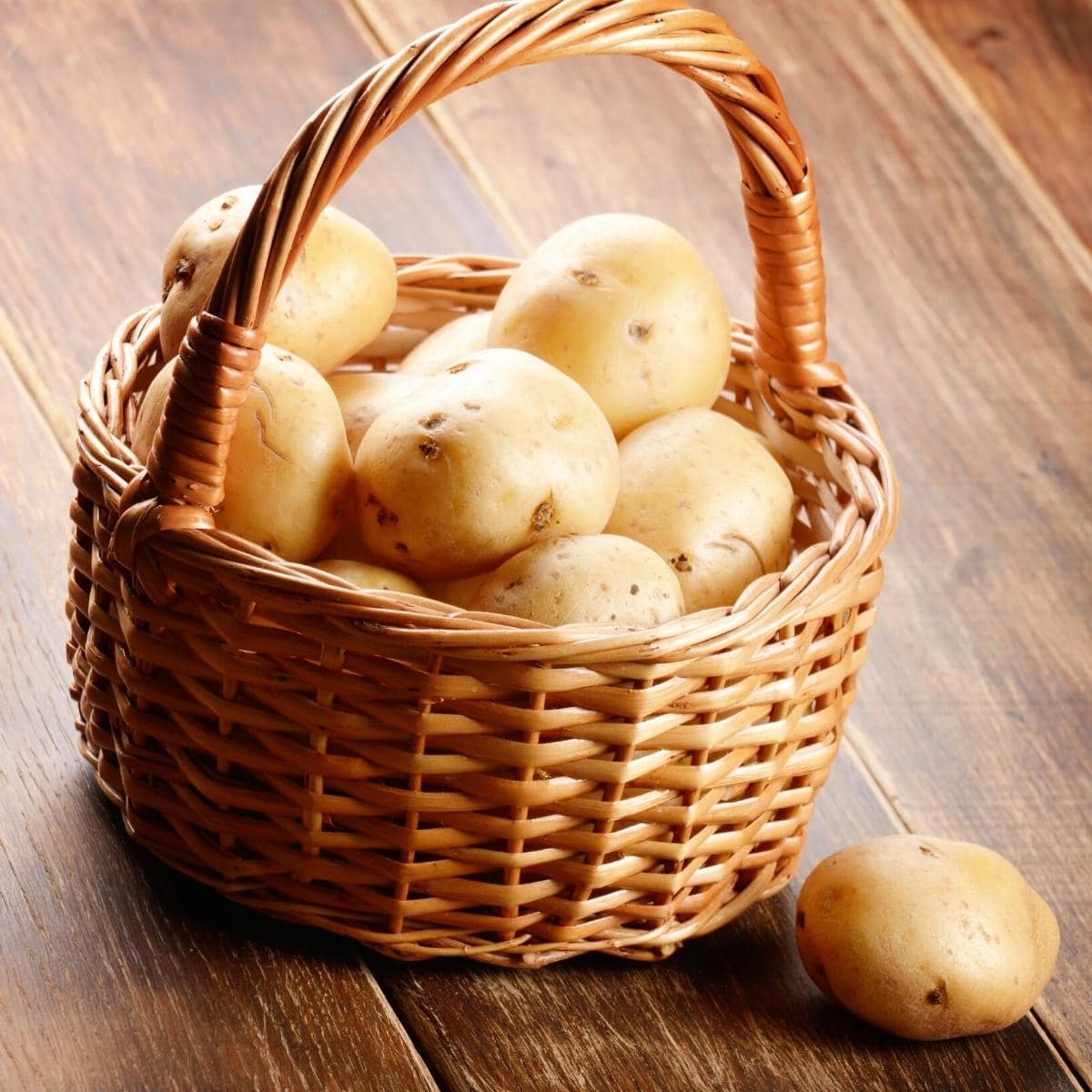 A large wooden basket filled with golden potatoes.