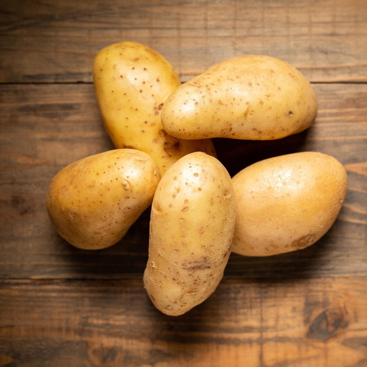 A wooden table with a stack of golden potatoes resting on it.