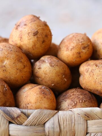 A small wooden basket filled with light brown potatoes.