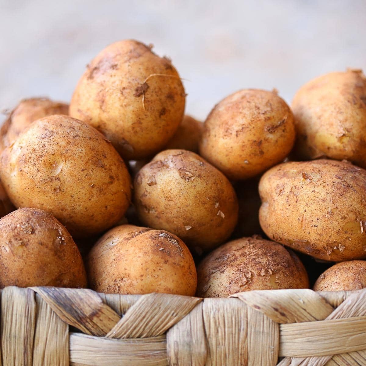 A wooden basket filled with light brown potatoes.