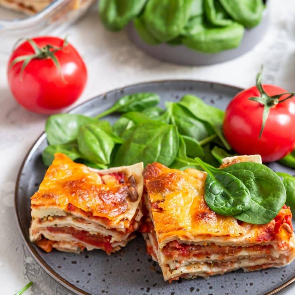 slices of vegetarian lasagna on a ceramic plate with various side dishes.