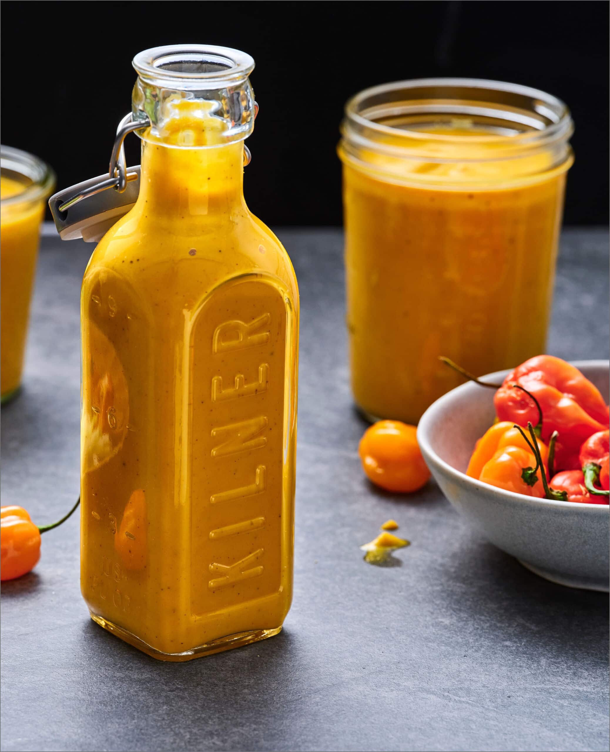 Open clear glass bottles filled with an orange sauce.