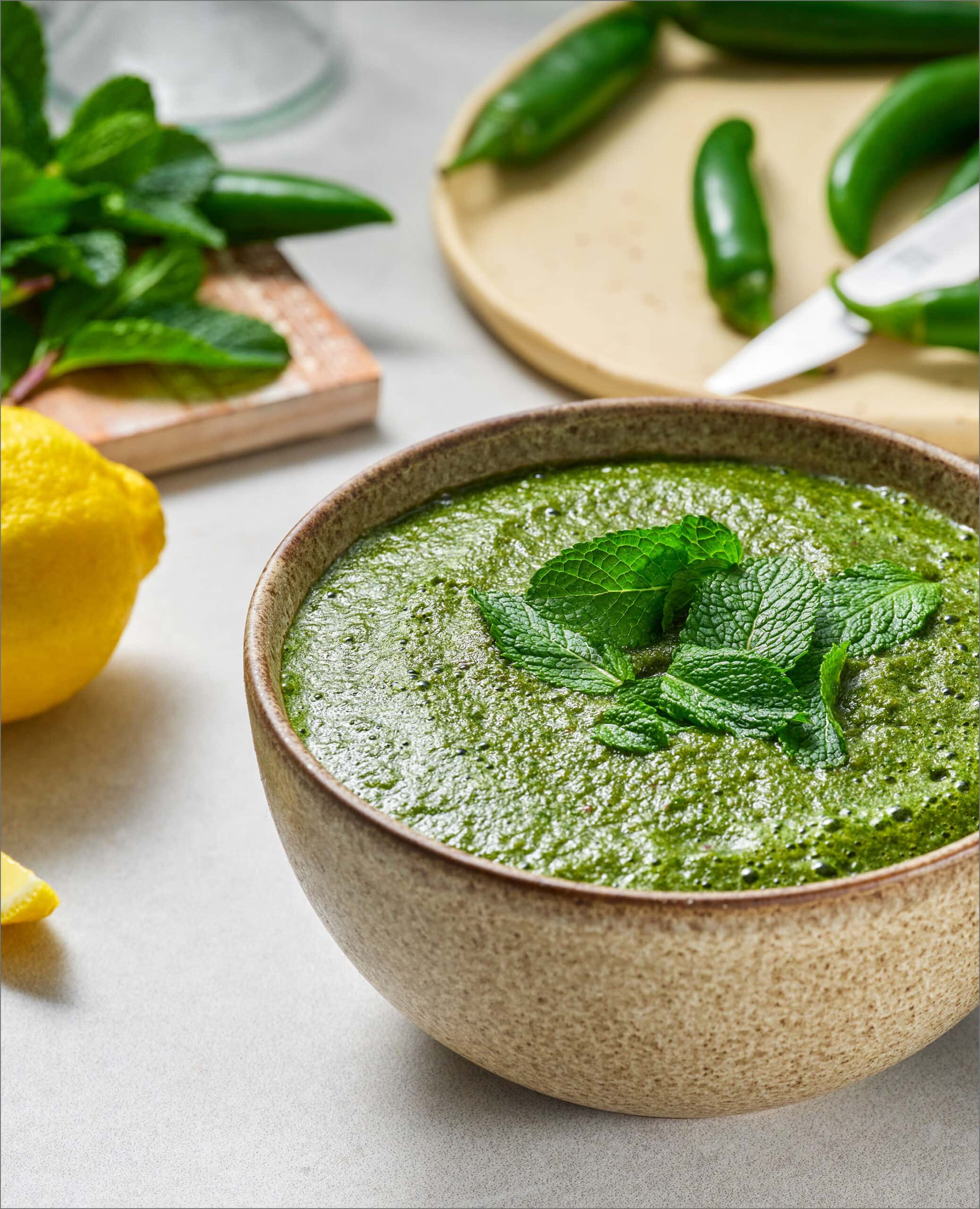 A brown ceramic bowl fill with a green sauce topped with fresh mint leaves.