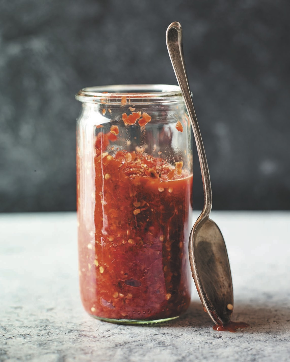 A clear jar filled with blended chiles with a spoon resting against it.