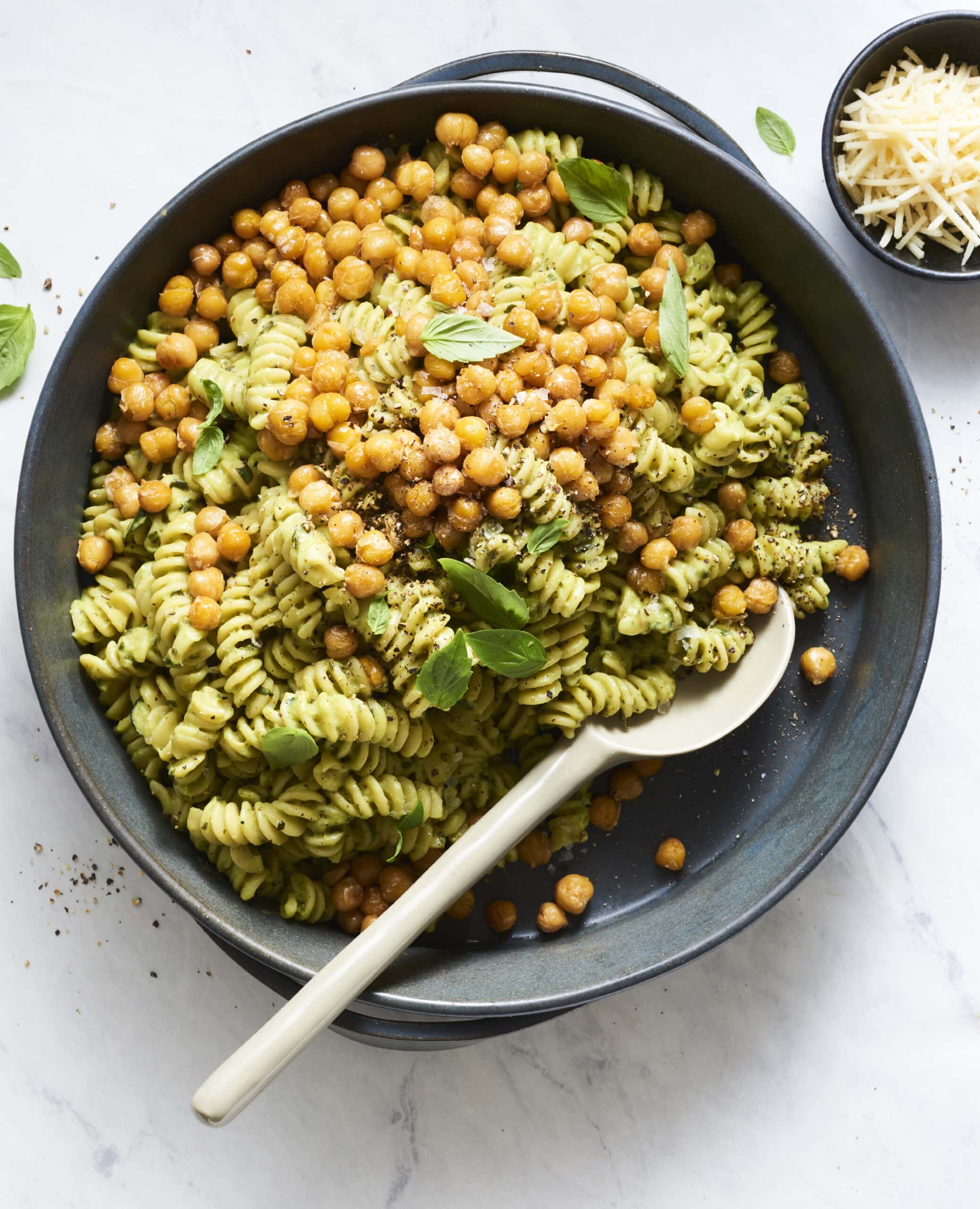 A large gray spoon scooping into a cast iron skillet filled with pesto pasta and crispy chickpeas.