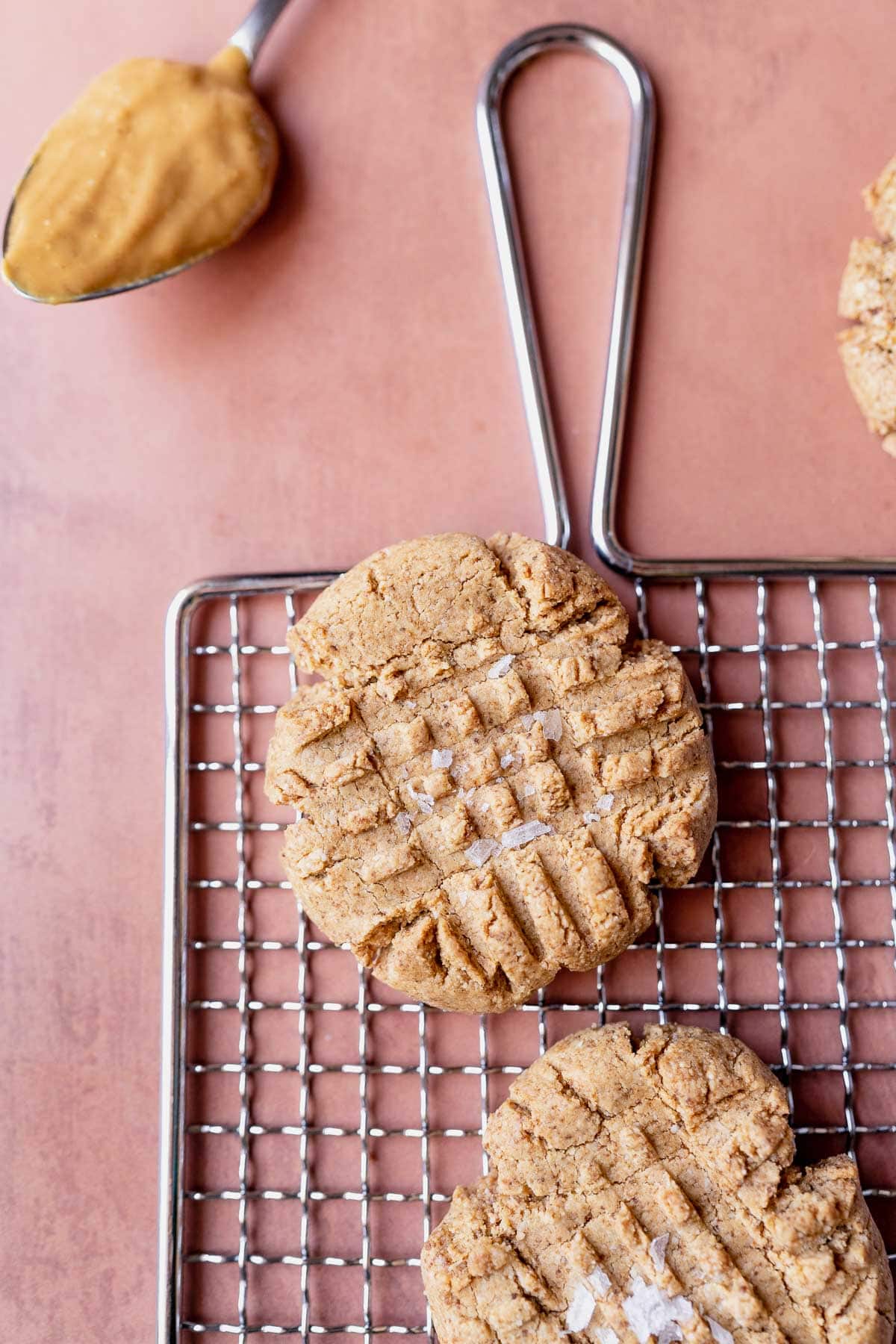 Close shot of a peanut butter cookie on silver rack on a pink table.