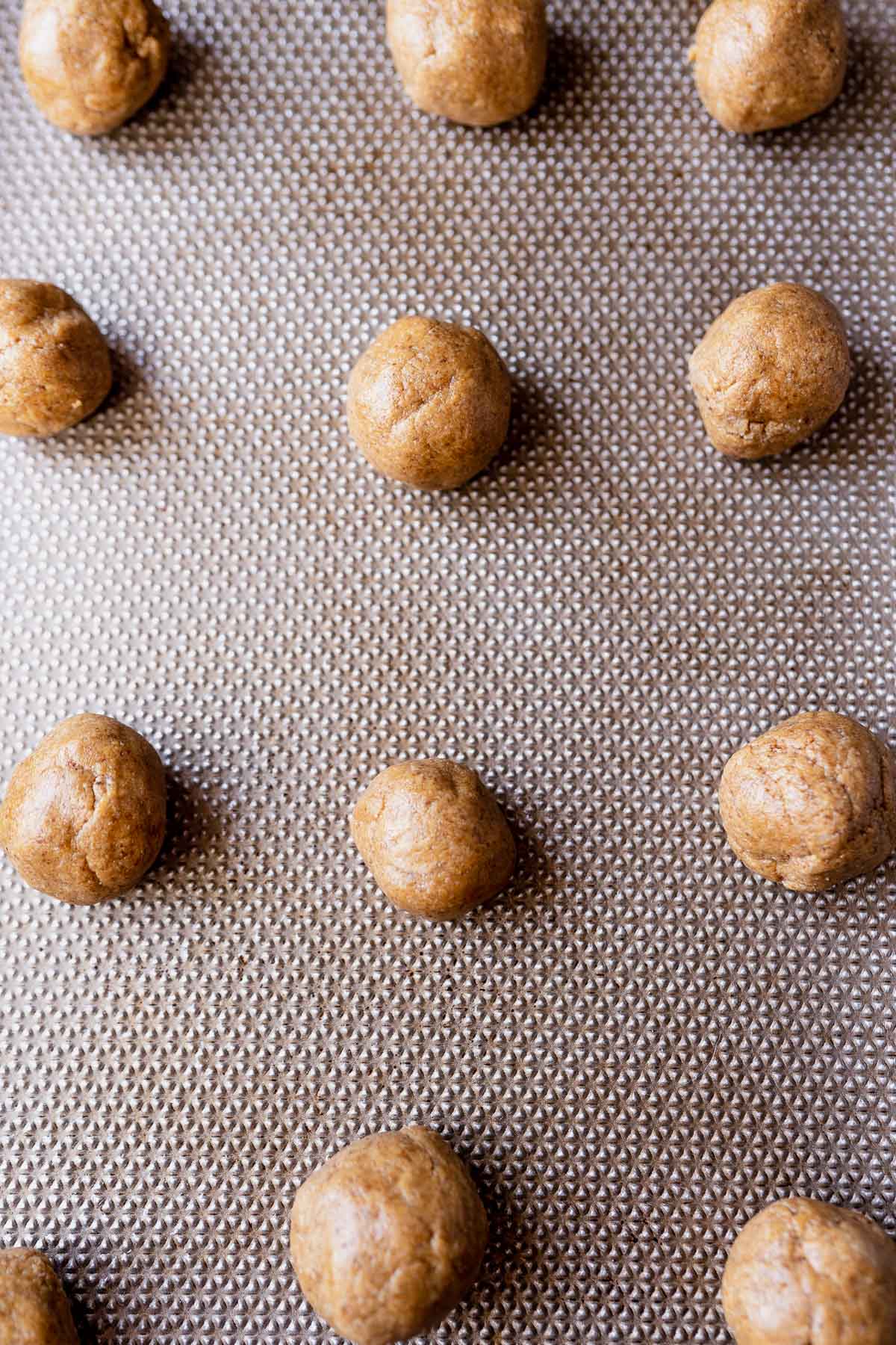 A silver textured baking sheet topped with rounds of tan dough.