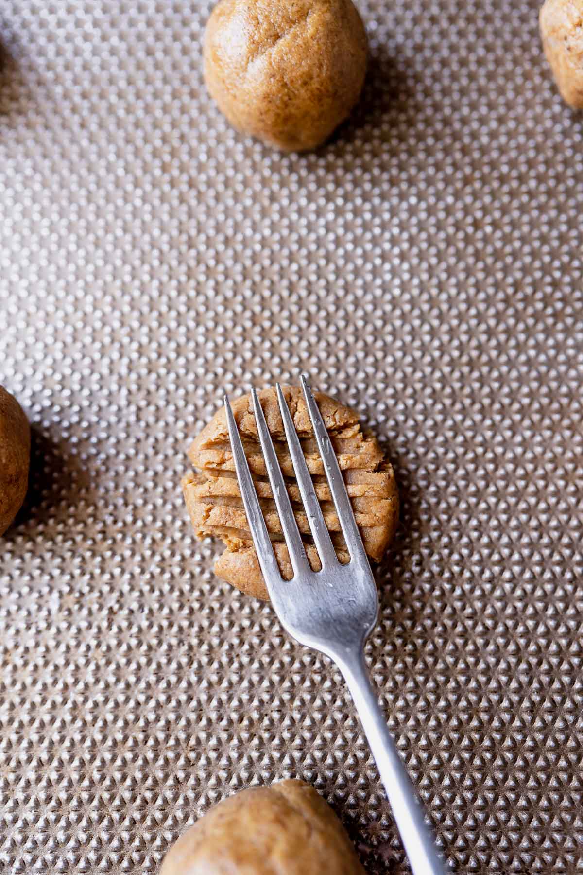 A fork pressing into cookie dough making a pattern.