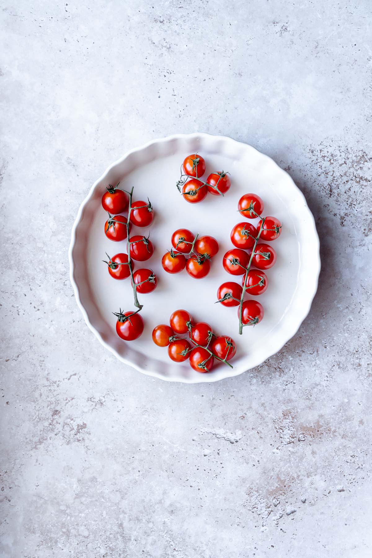 A white dish filled with plump red cherry tomatoes on the vine.