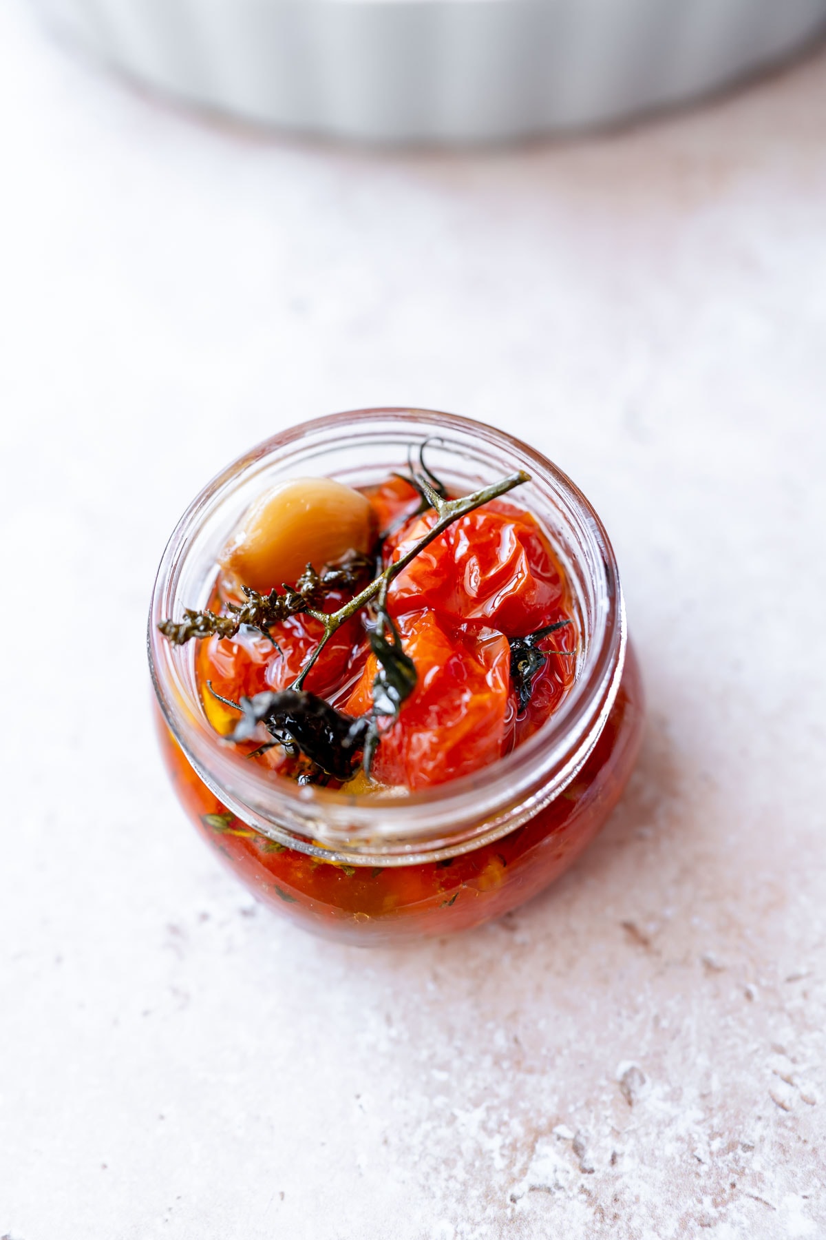 An open clear jar filled with soft red cherry tomatoes on the vine.
