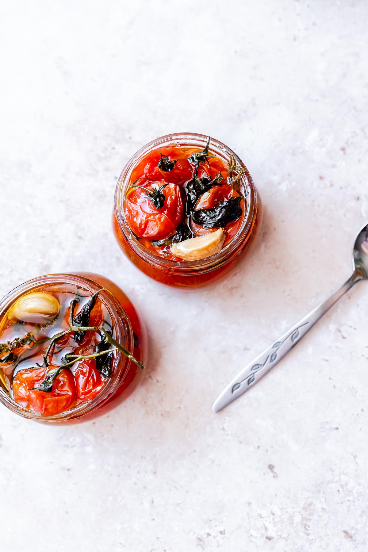 Two clear open glass jars filled with oil and softened tomatoes.