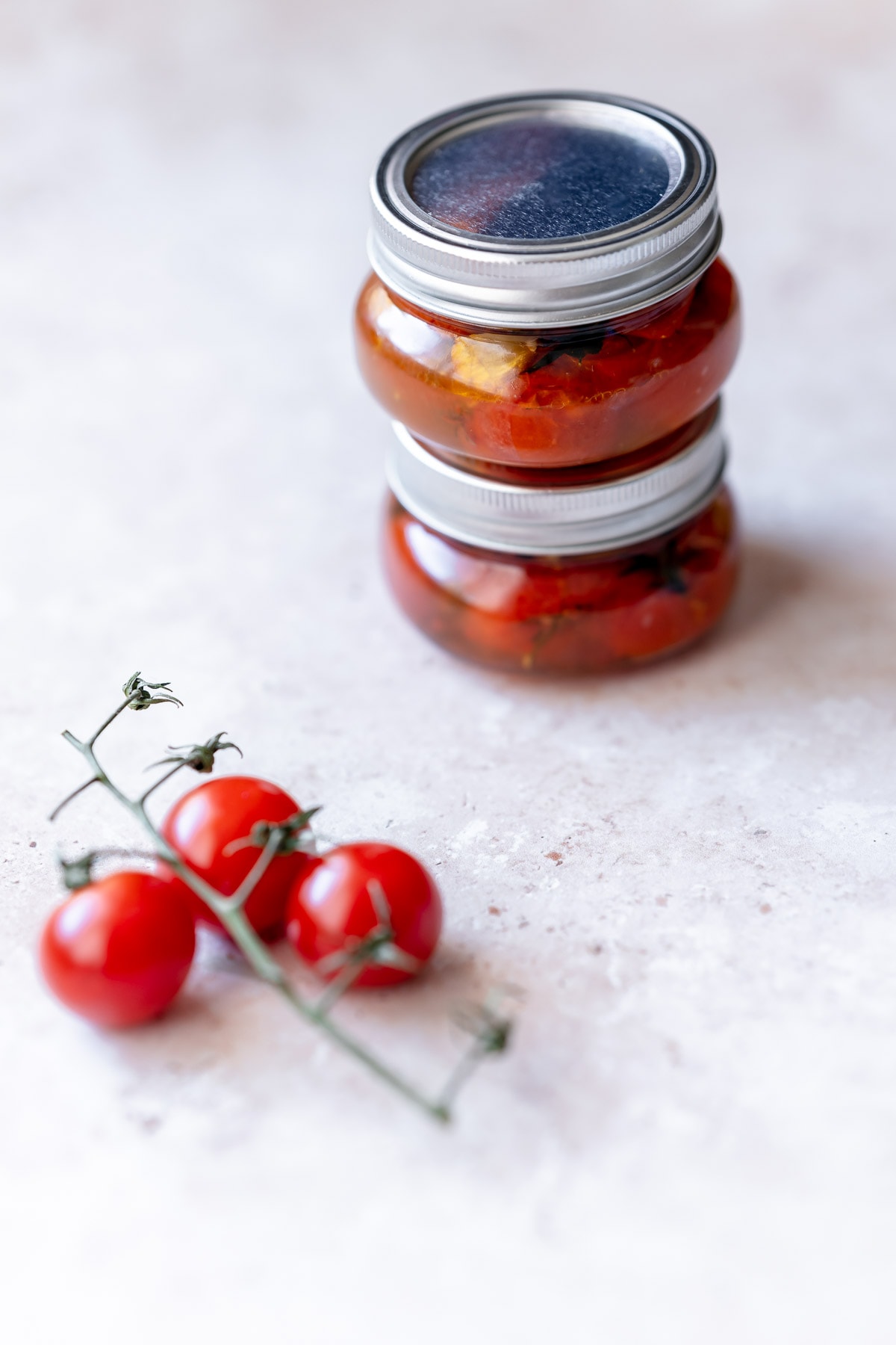 Two clear stacked jars filled with red tomatoes in oil.