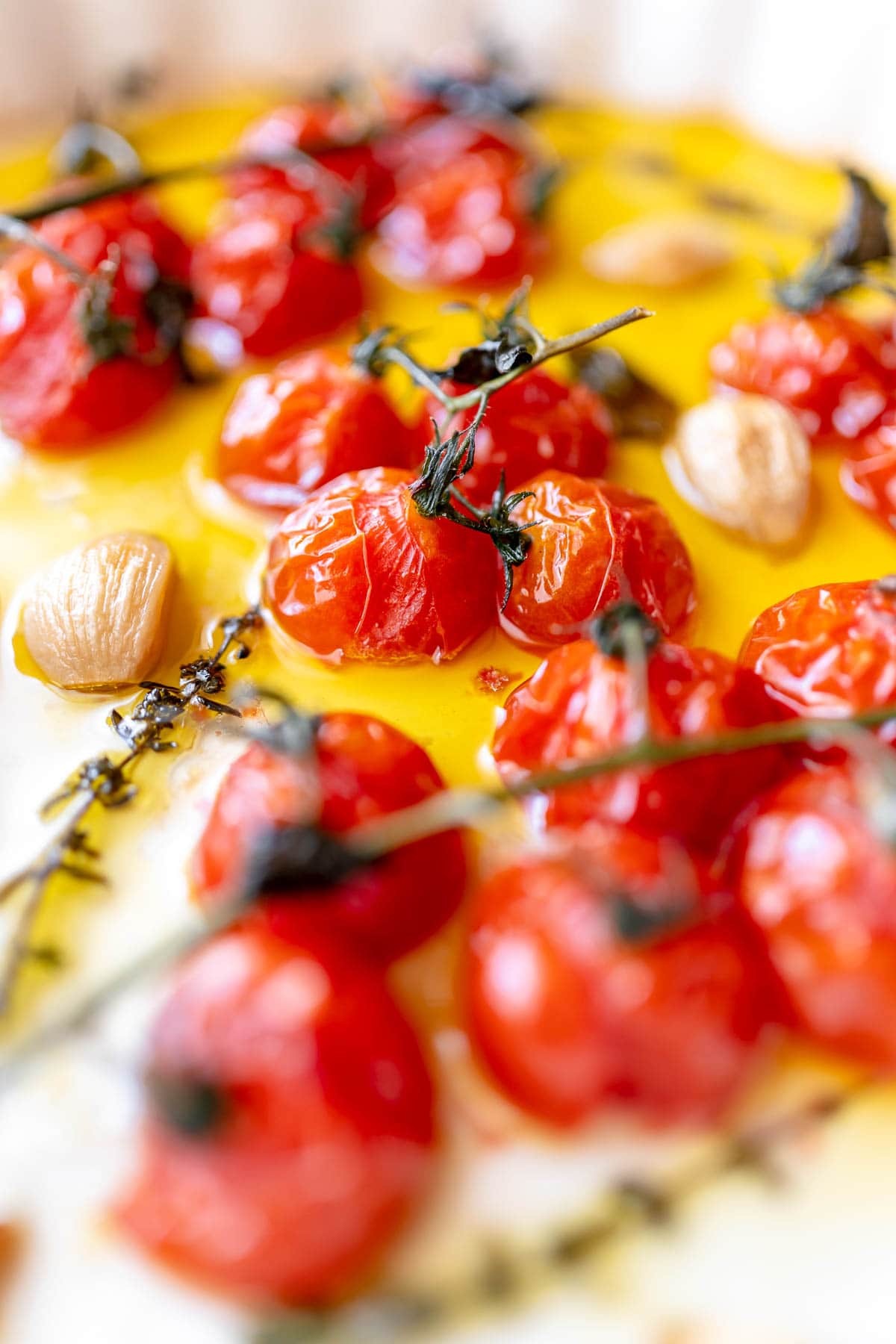 Close shot of softened cherry tomatoes on the vine resting in oil in a baking dish.