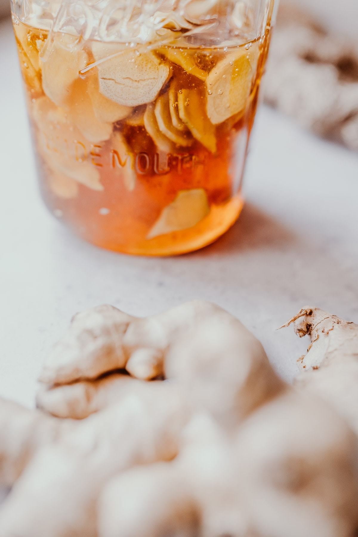 Side shot of a clear jar filled with golden honey and slices of ginger root.